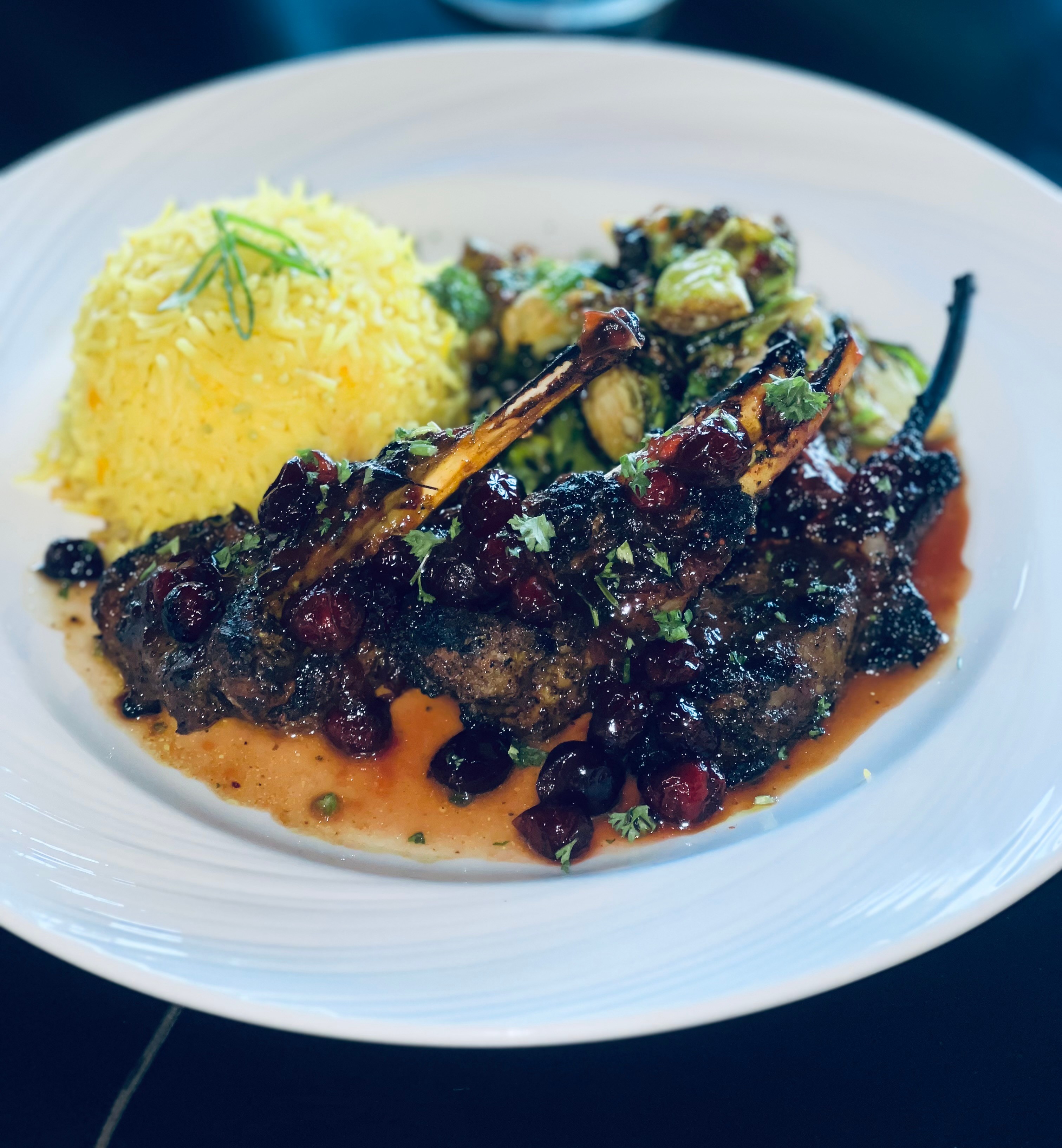Plate with grilled meat, yellow rice, and vegetable side dish, on a white plate.