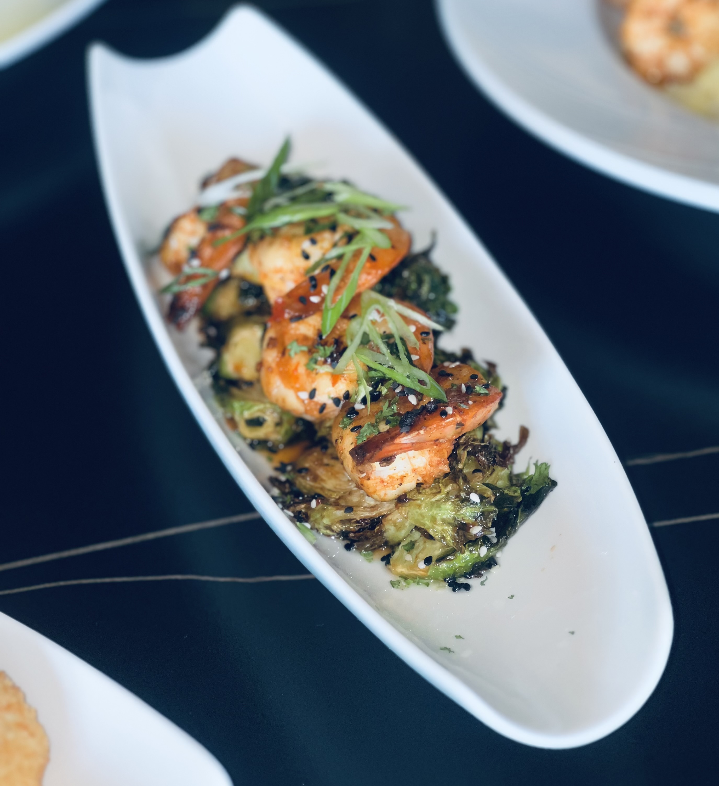 Grilled salmon with green garnish on a white oval plate, served on a dark surface.