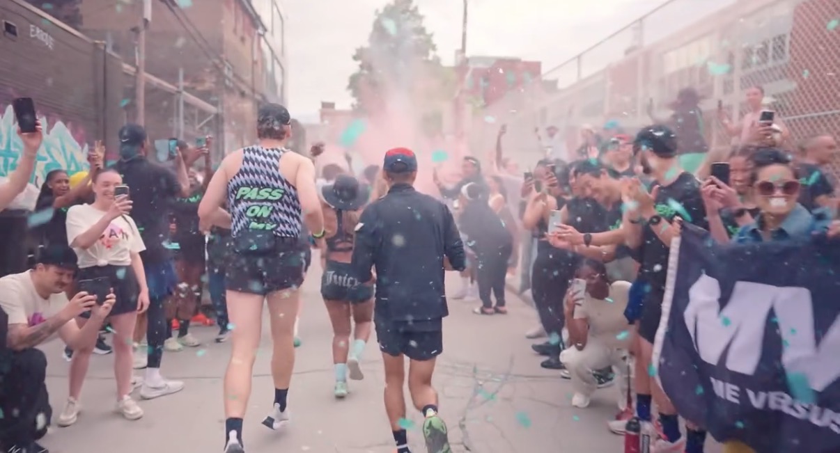 Crowd of people celebrating outdoors with colorful powder and confetti, some wearing sunglasses and casual clothing.