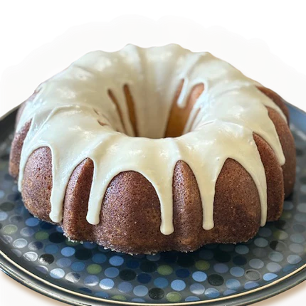 Bundt cake with white glaze on a decorative plate, dark background, close-up view.