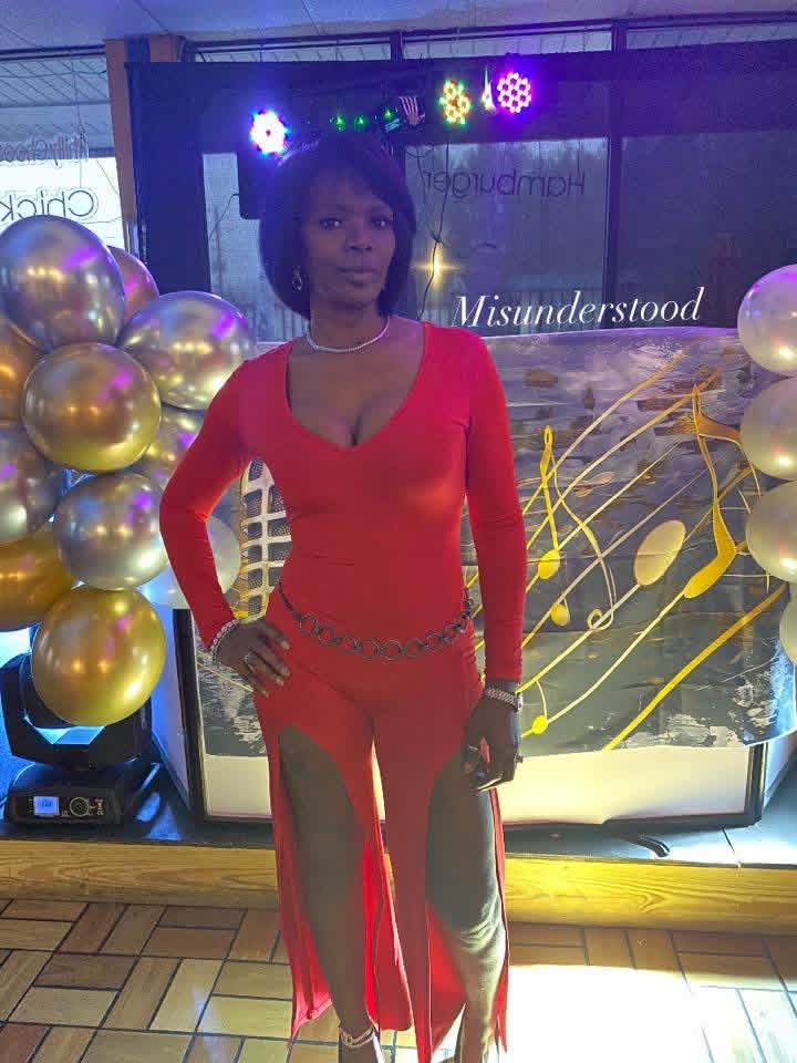 Woman in red dress standing in front of decorated backdrop with balloons and lights.