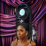 Woman with elaborate hairstyle and jewelry in front of colorful draped fabric backdrop.