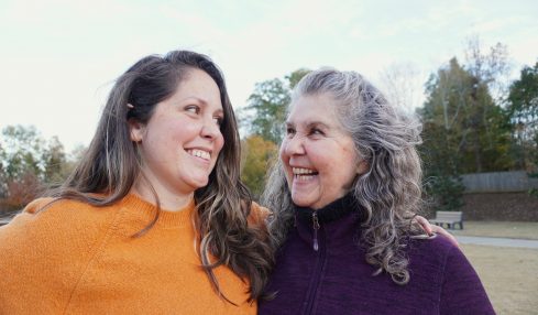 Two women smiling and looking at each other outdoors on a sunny day.