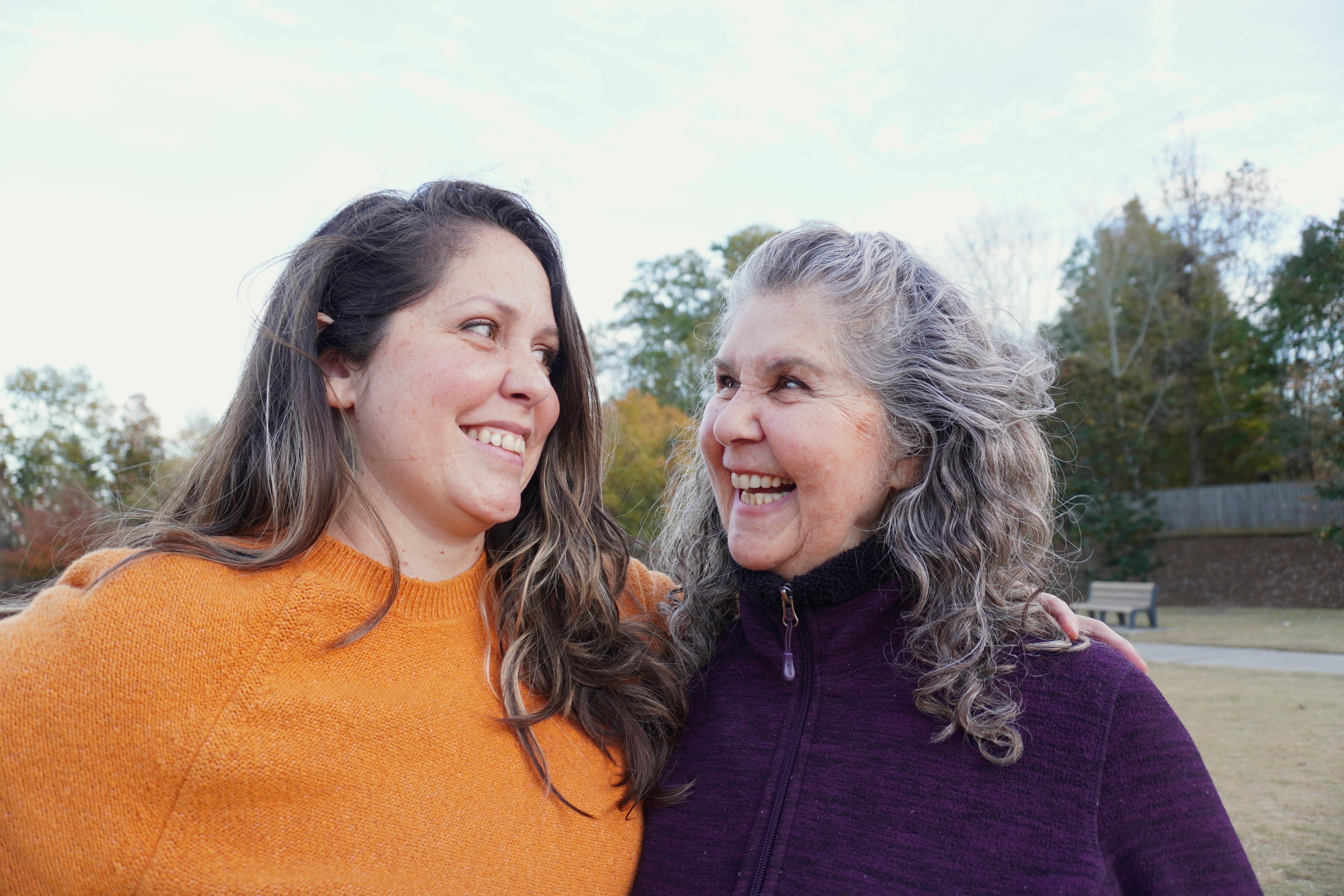 Two women smiling and looking at each other outdoors on a sunny day.