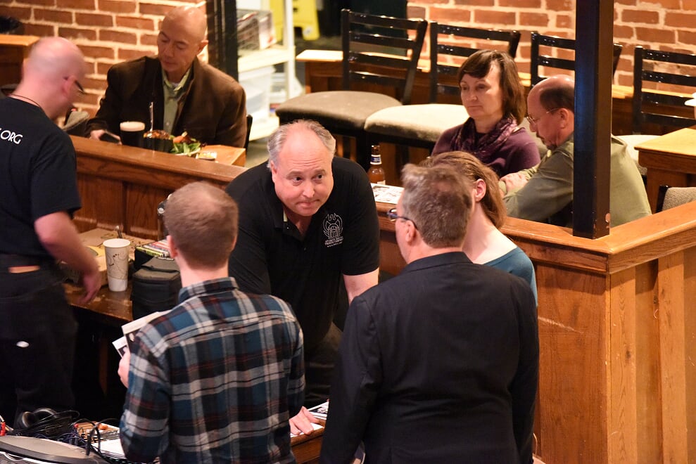 Group of people talking in a restaurant with brick wall background and wooden furniture.