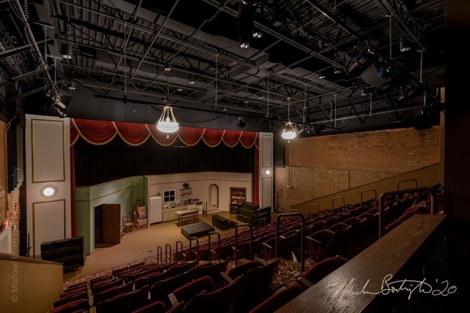 Theater stage with red curtains, white walls, and seating area, viewed from an elevated angle.