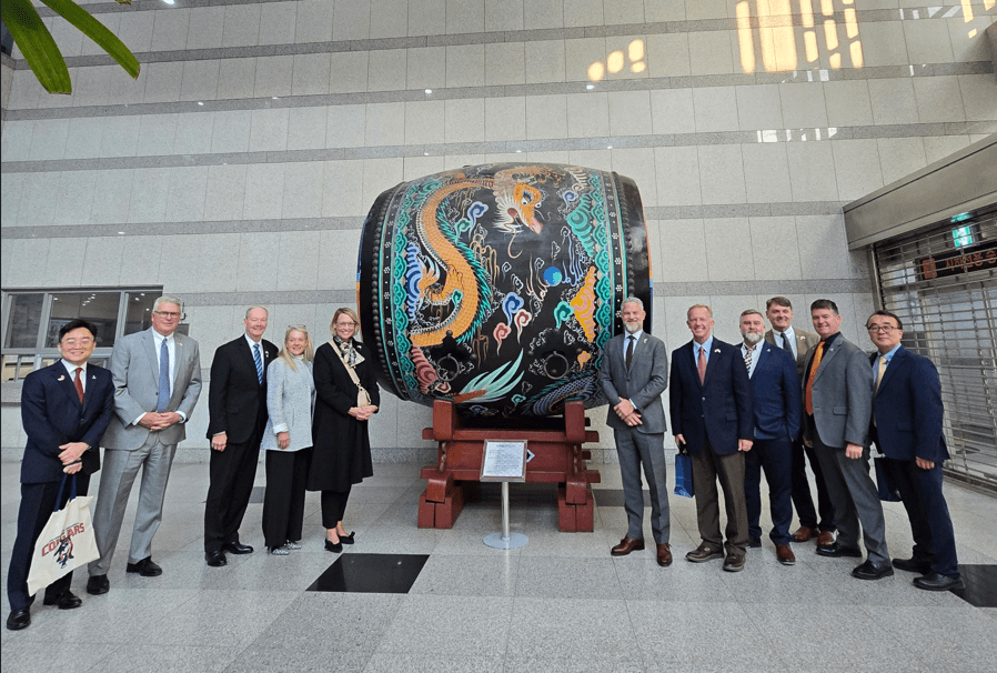 Group of people standing beside a large, decorated drum on a stand in a modern indoor space.