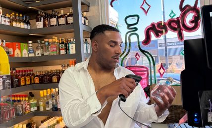 Person taking a mirror selfie in a store, holding a phone, with shelves and colorful items in the background.