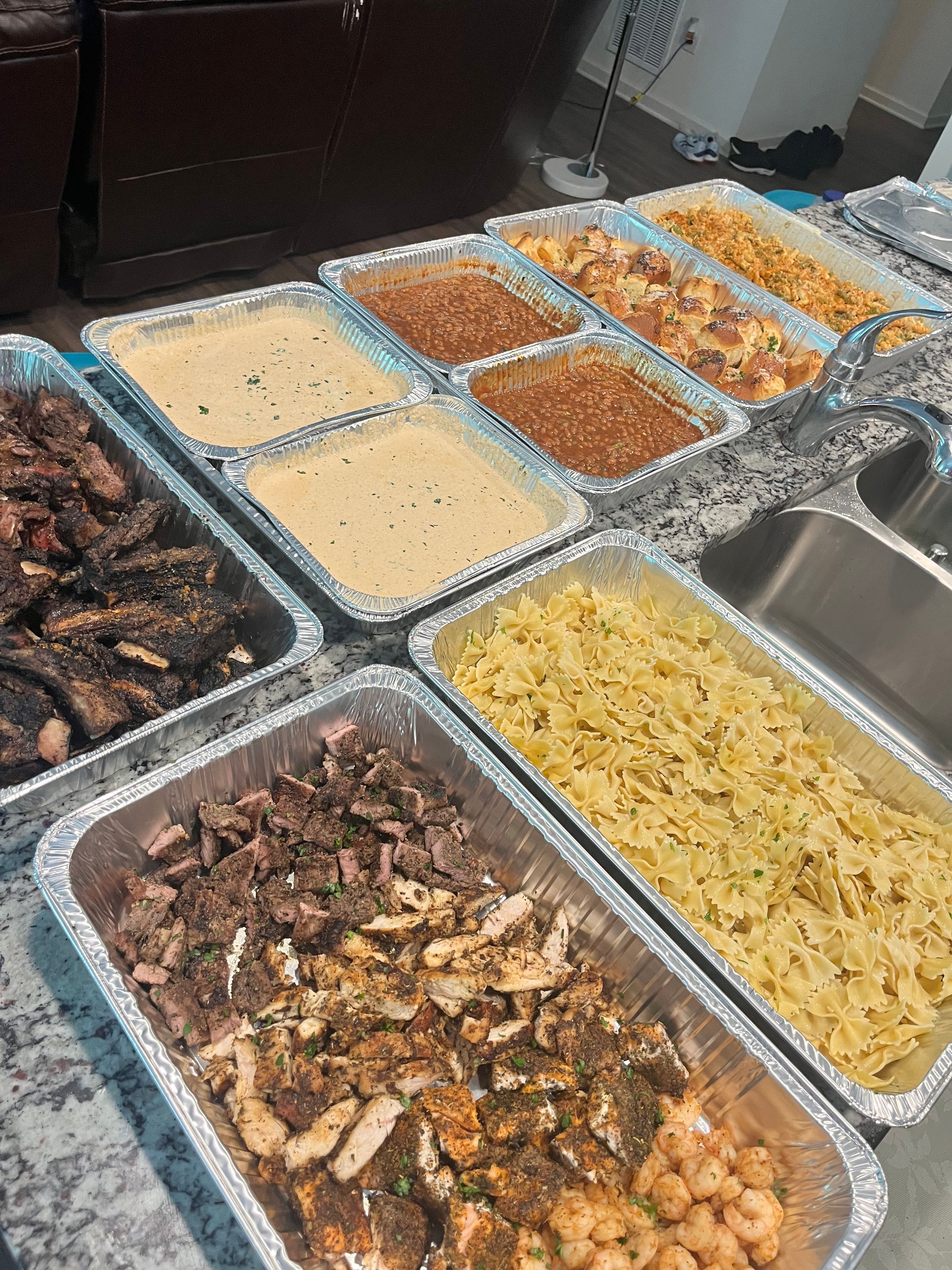 Various dishes in aluminum trays, including shredded cheese, cooked meat, and sauces, on a kitchen counter.