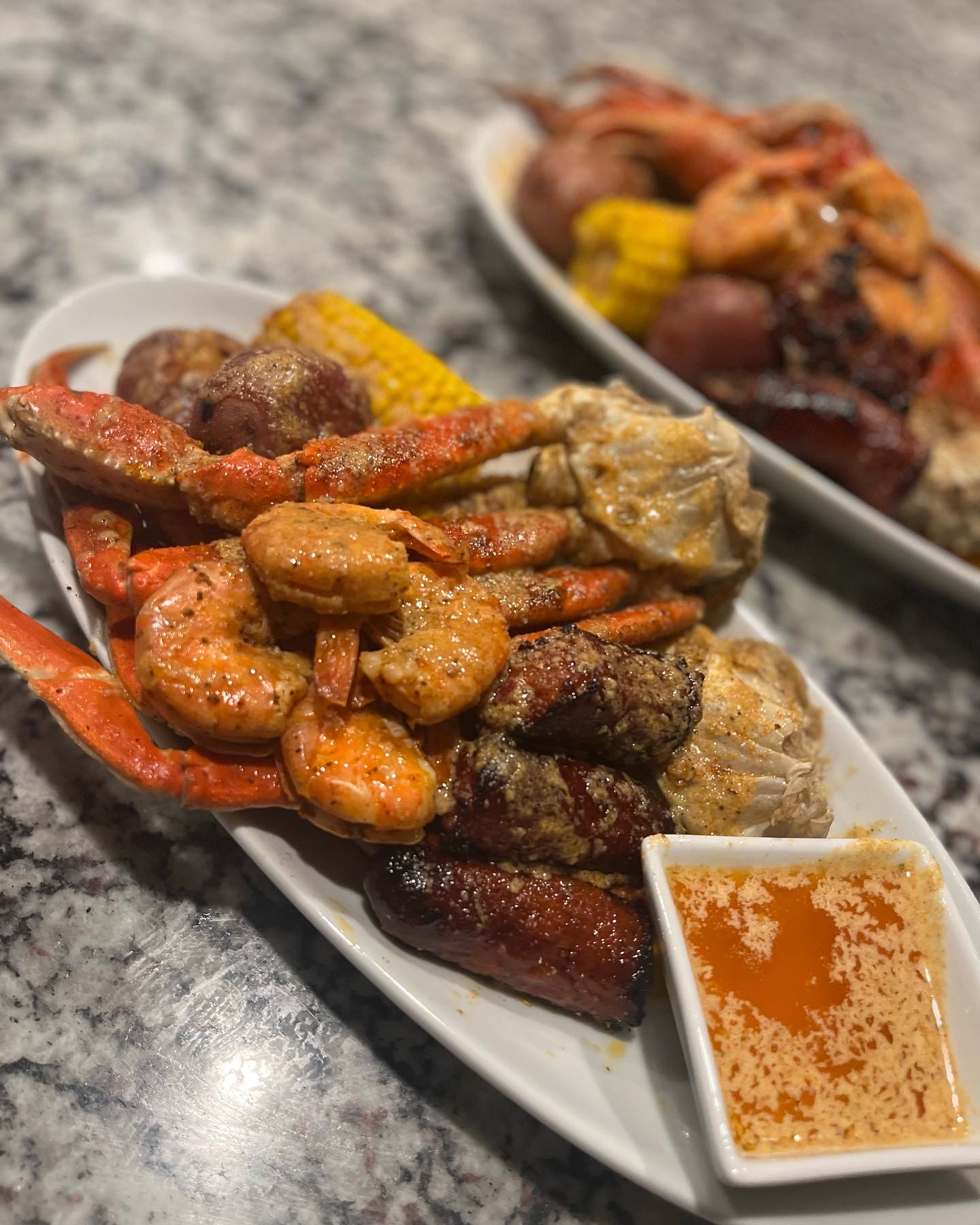 Assorted cooked seafood and meat dishes on a white platter with dipping sauce, on a gray marble surface.