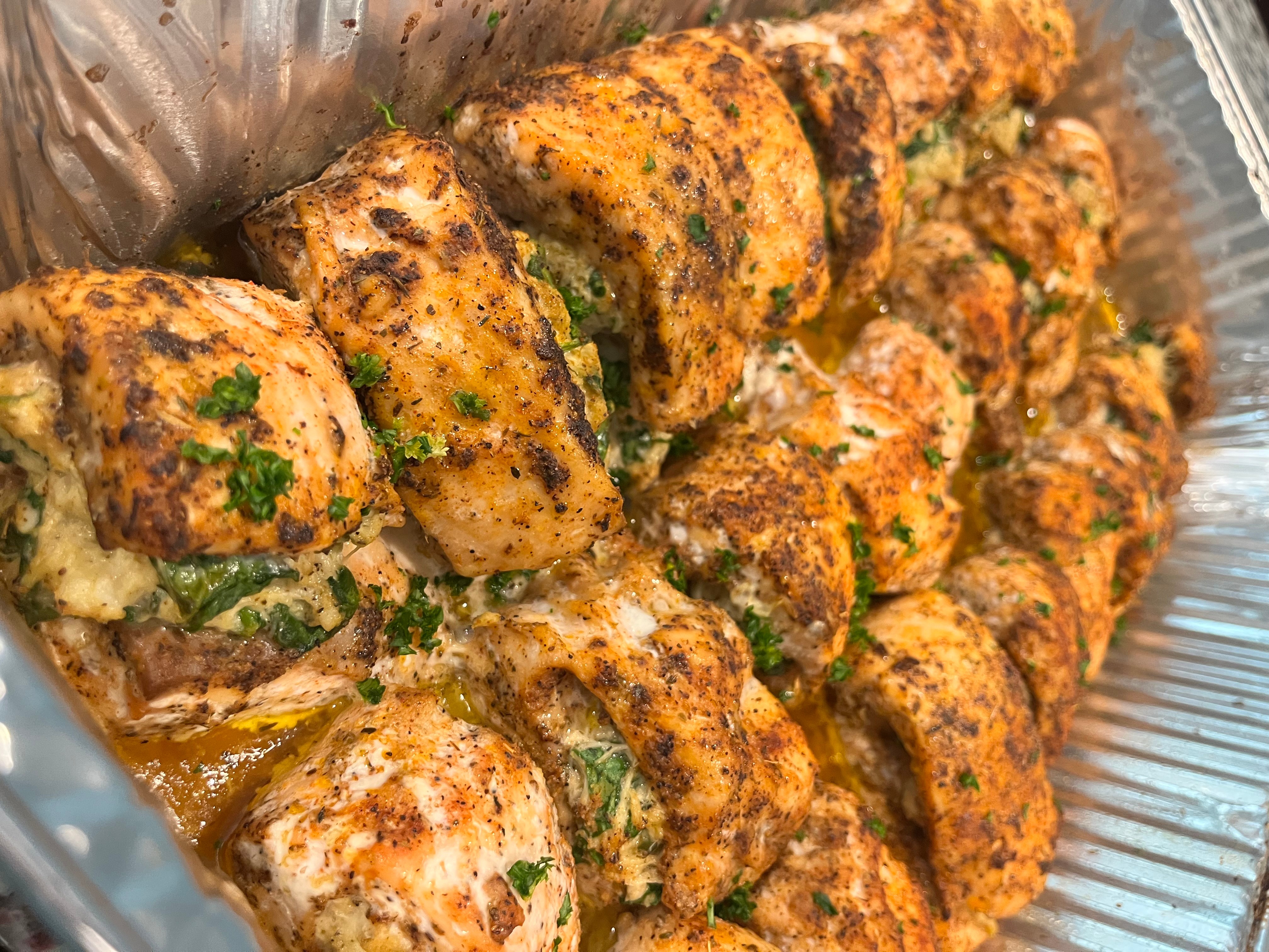 Close-up of grilled chicken skewers with herbs and spices, arranged in a row inside a container.