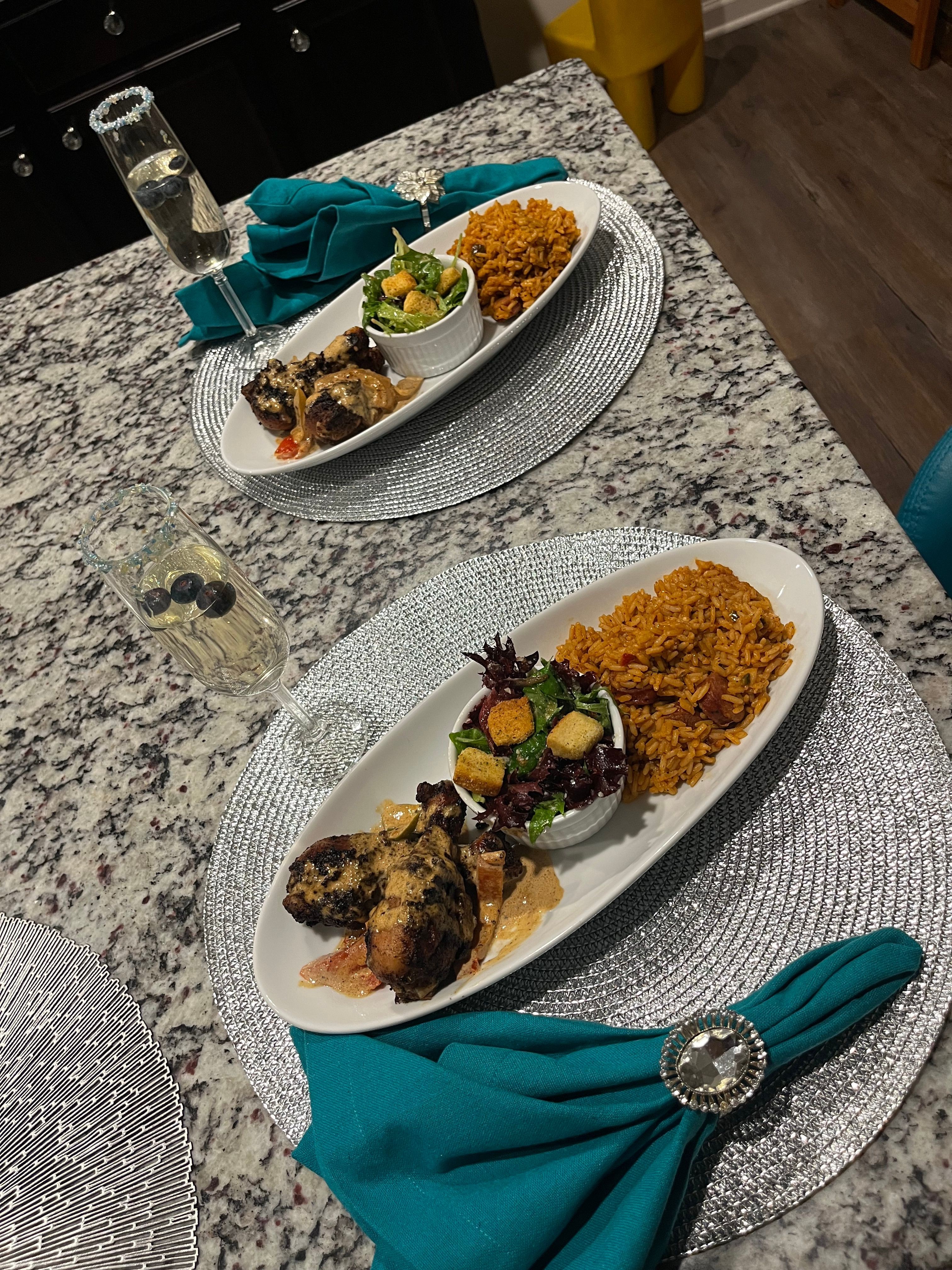 Two plates of food on a granite table with teal napkins, glasses, and a small bowl of lime, viewed from above.