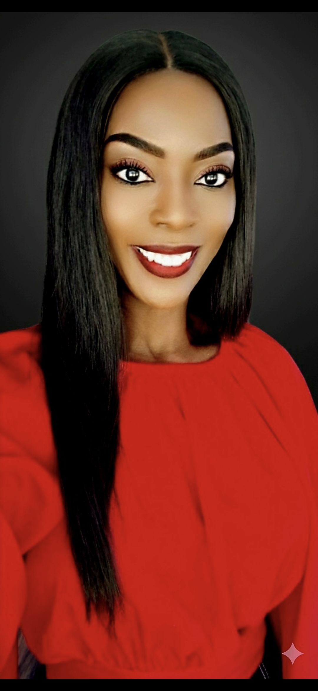 Young woman with long black hair, smiling, wearing a red top, against a dark background.