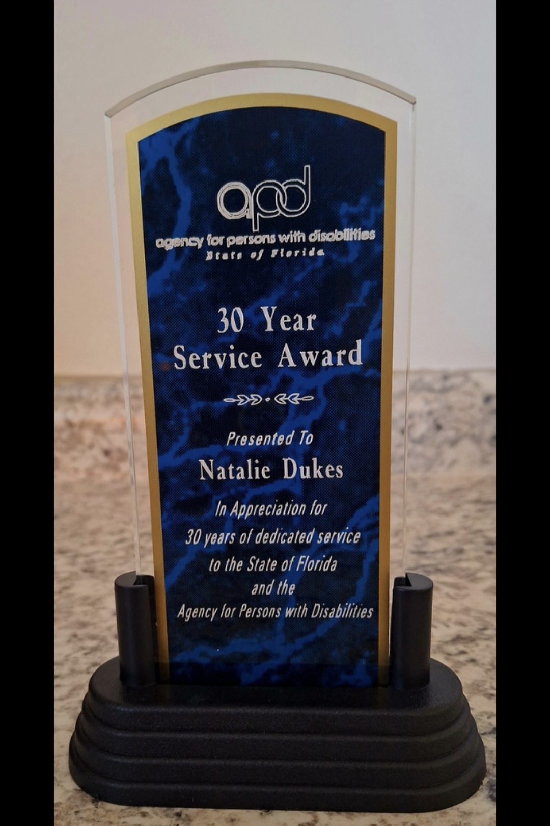 Blue award plaque with gold border, recognizing 30 years of service, presented to Natalie Dukes, with black base.