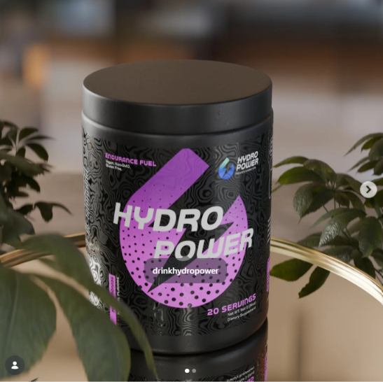 Black container with purple and white label, surrounded by green plants, on a reflective surface.