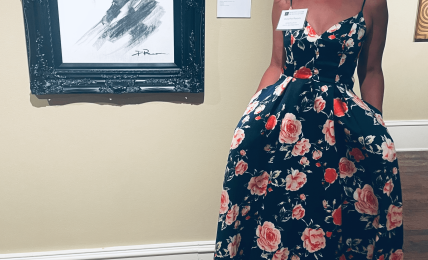 Woman in a floral dress standing next to a framed black and white portrait in an art gallery.