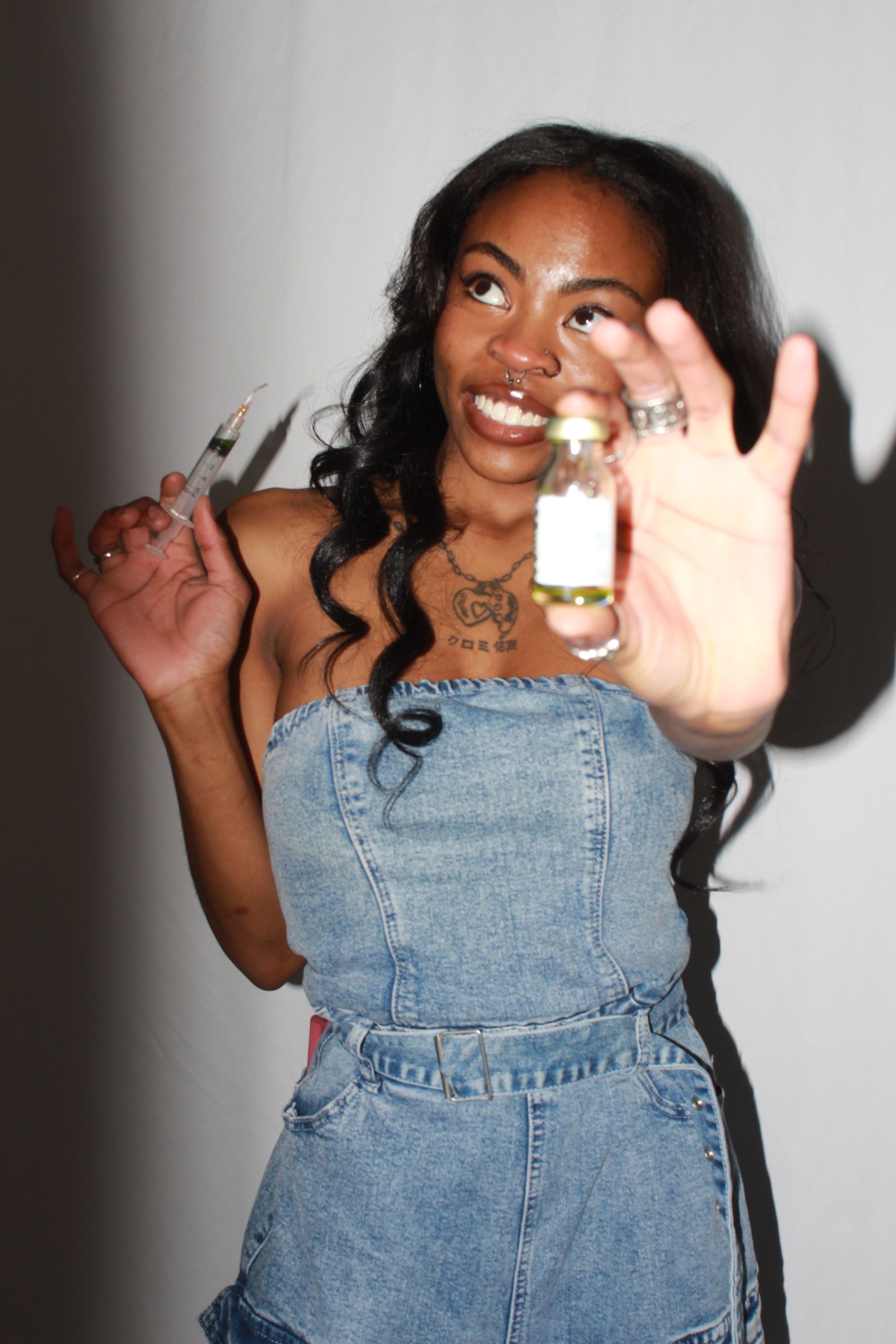 Woman with long curly hair smiling, holding a phone, wearing a denim dress, lying on a white surface.