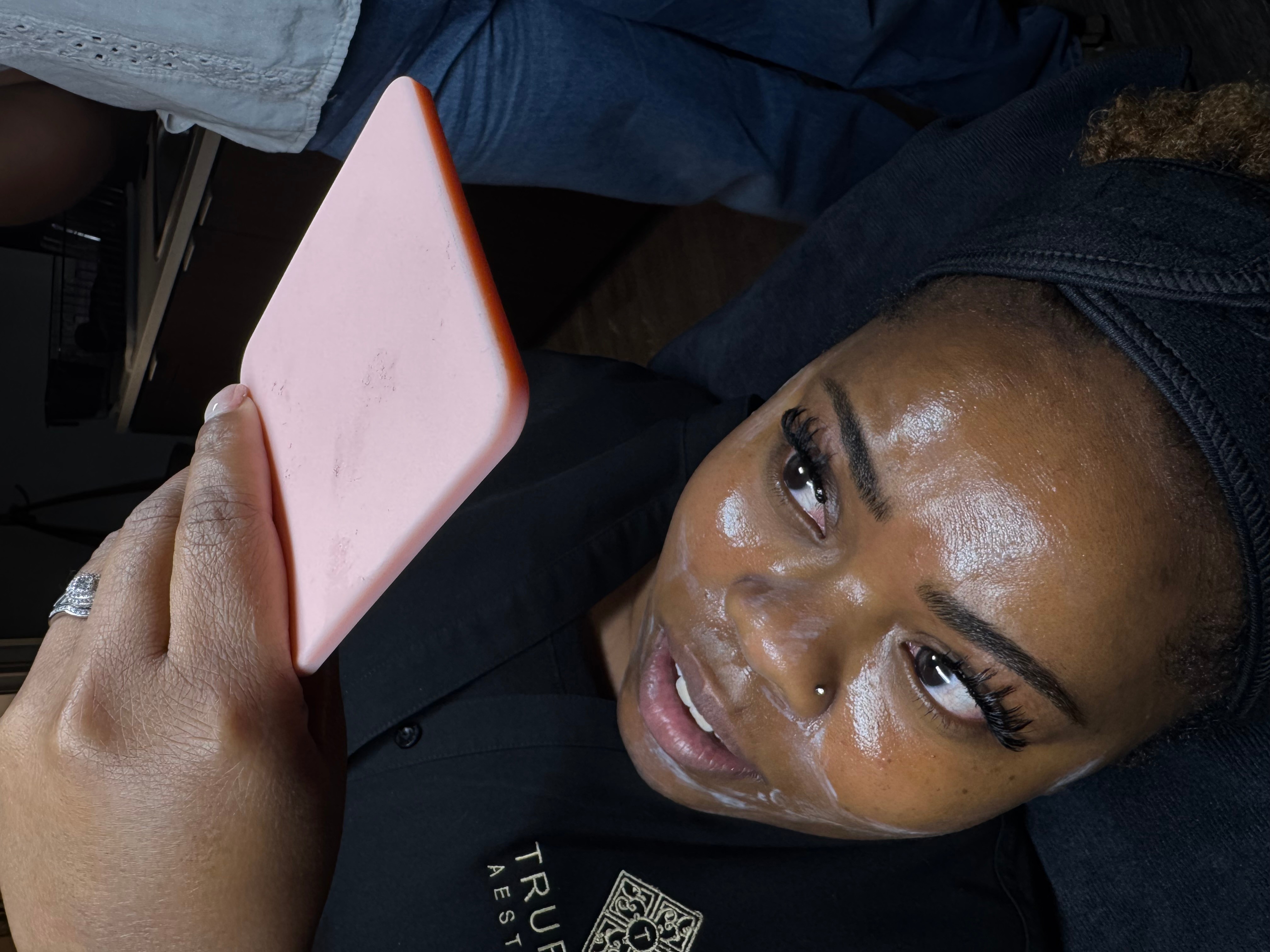 Close-up of a woman with a headband looking at a pink phone, with tears on her face.