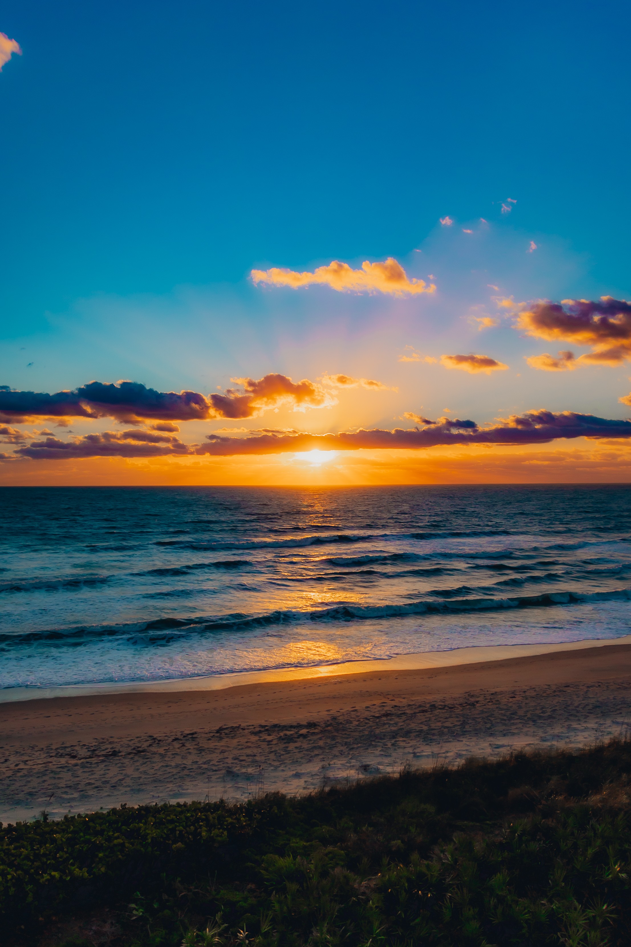 Sunset over the ocean with colorful clouds and a sandy beach foreground.