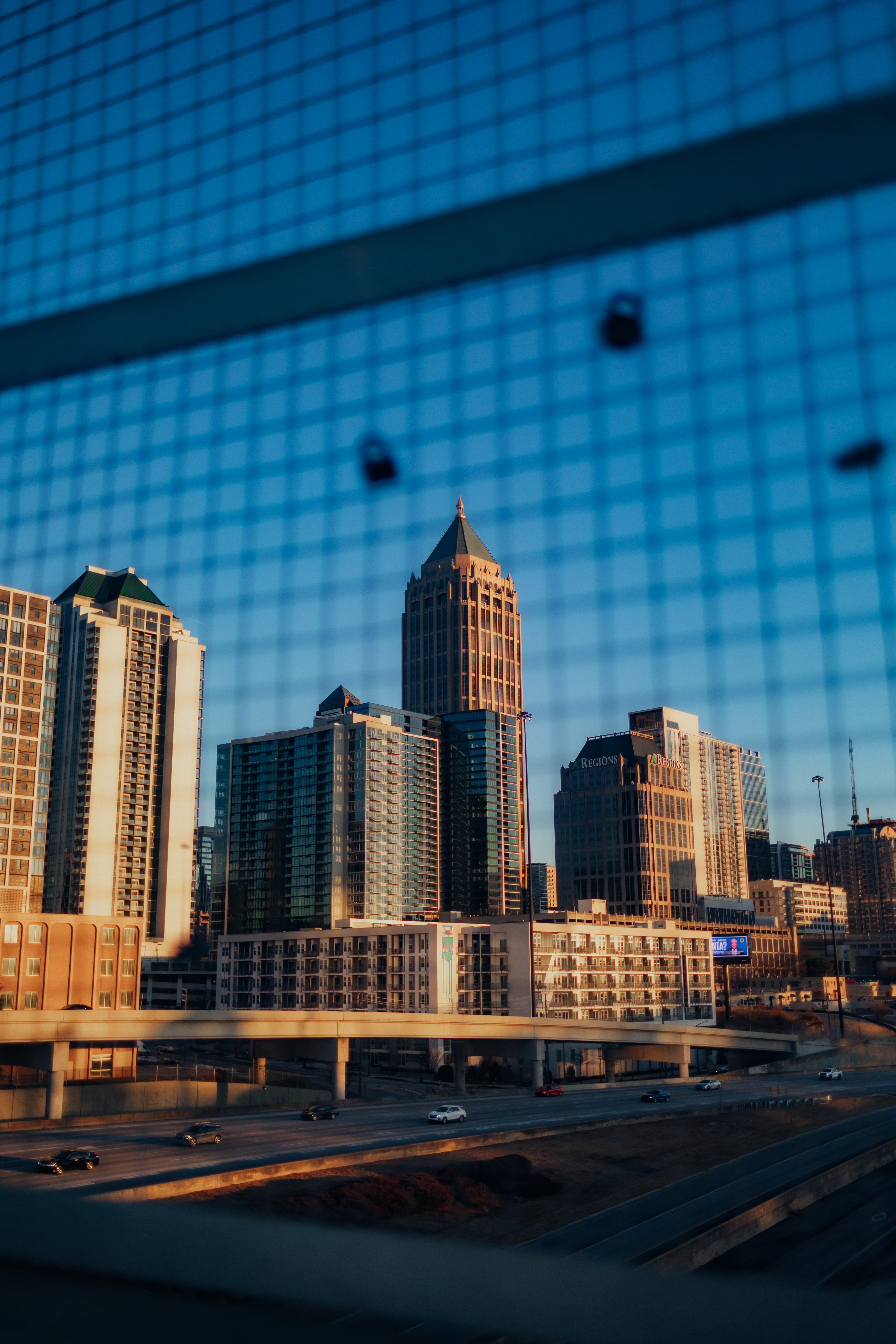 City skyline with tall buildings seen through a window with a grid pattern, reflecting the sky and cityscape.