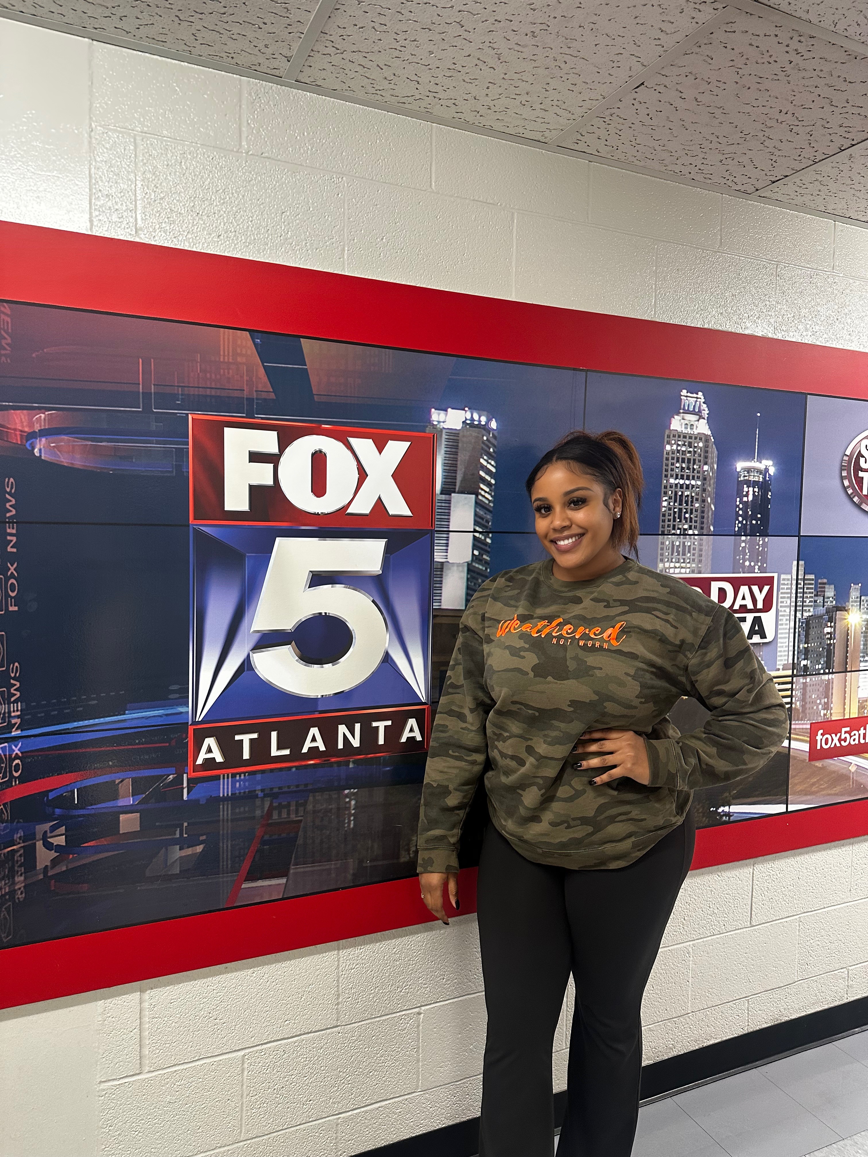 Woman standing next to a FOX 5 Atlanta news display, smiling, in an indoor setting.
