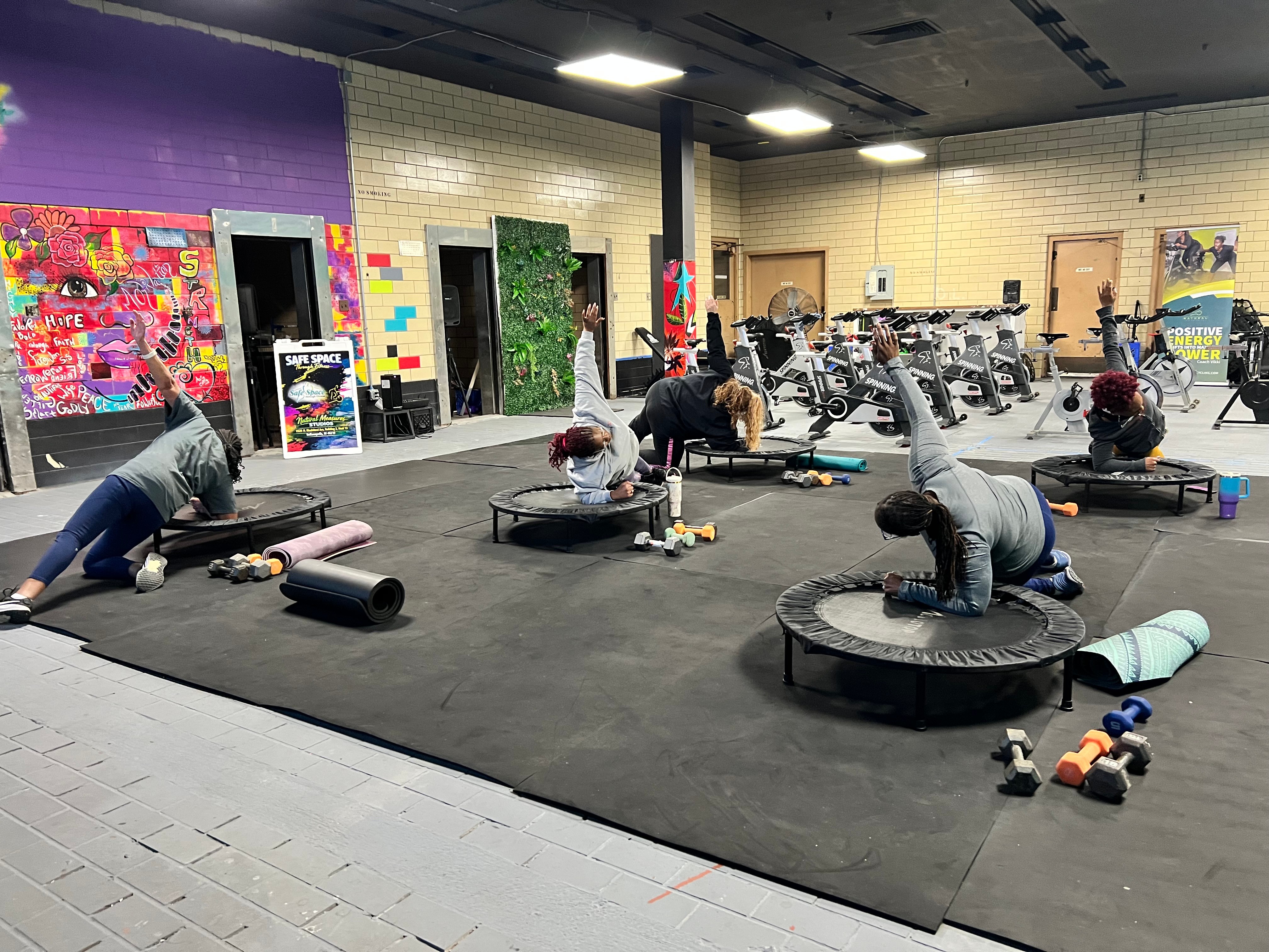 People exercising on mats and trampolines in a gym with colorful walls and exercise equipment in the background.