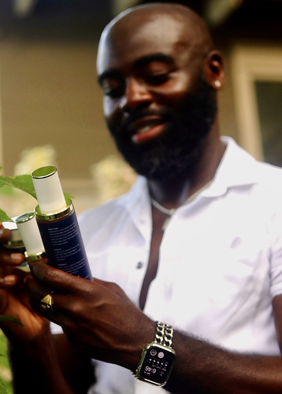 Man with a beard and white shirt holding two bottles, smiling, with a blurred background.