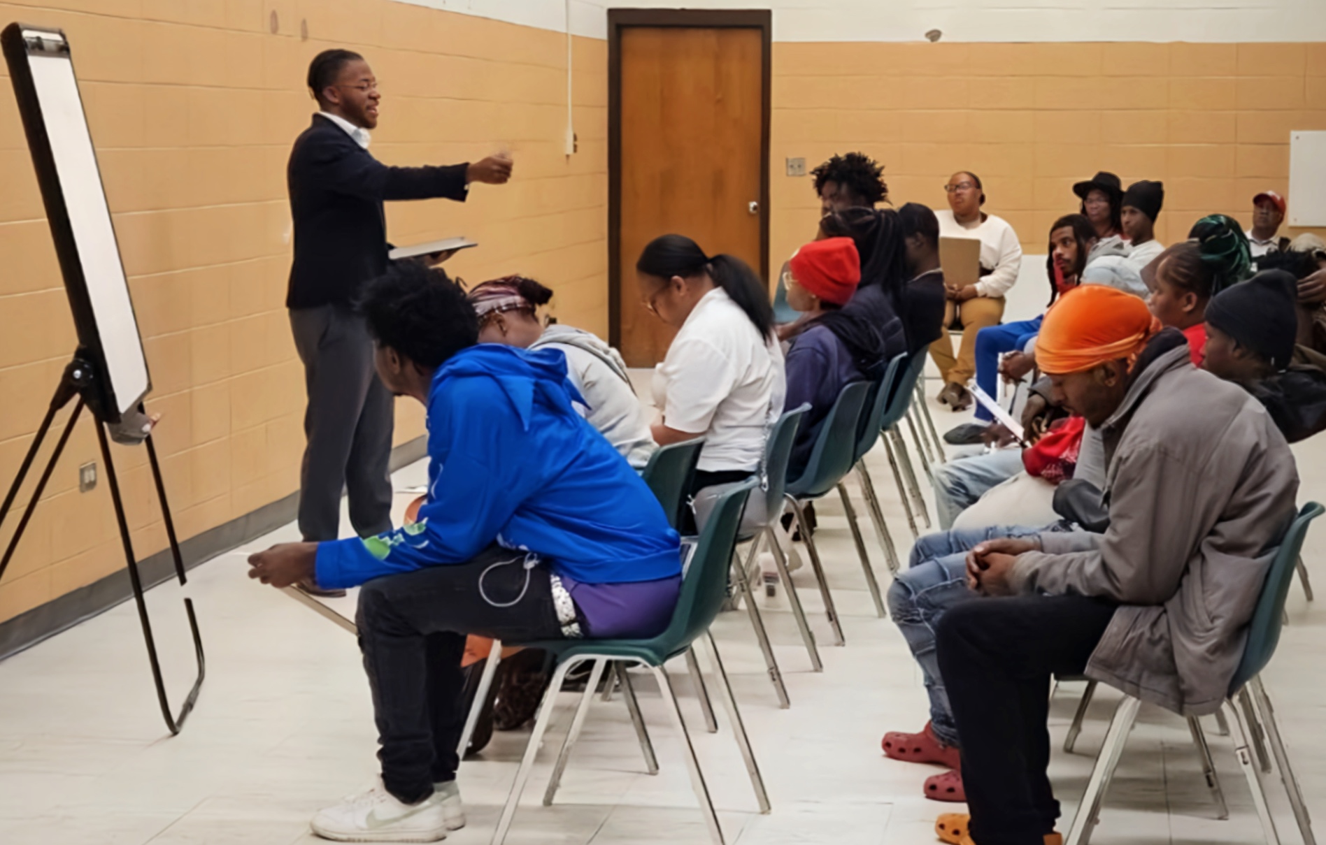 Person standing and speaking to seated group in a classroom or seminar setting.