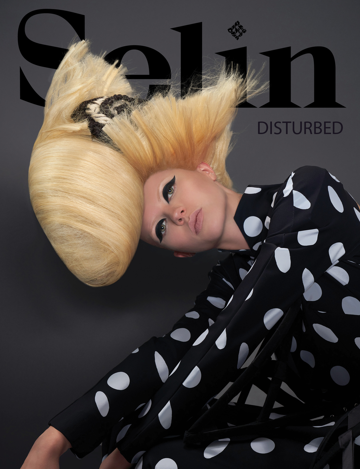 Woman with platinum blonde hair styled in a large updo, lying on a black background with text, wearing a polka dot outfit.
