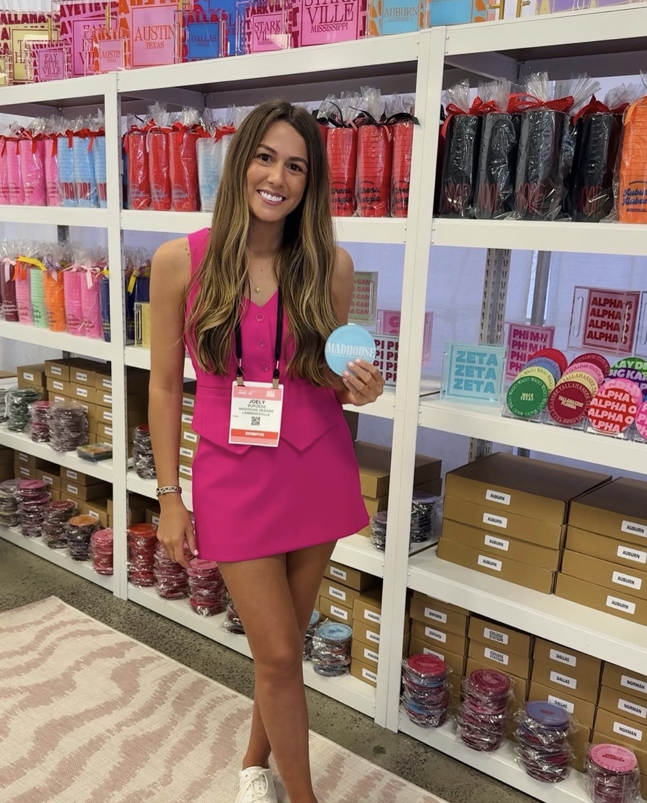 Young woman with long hair in a pink dress holding a small blue item in a store aisle with colorful products on shelves.