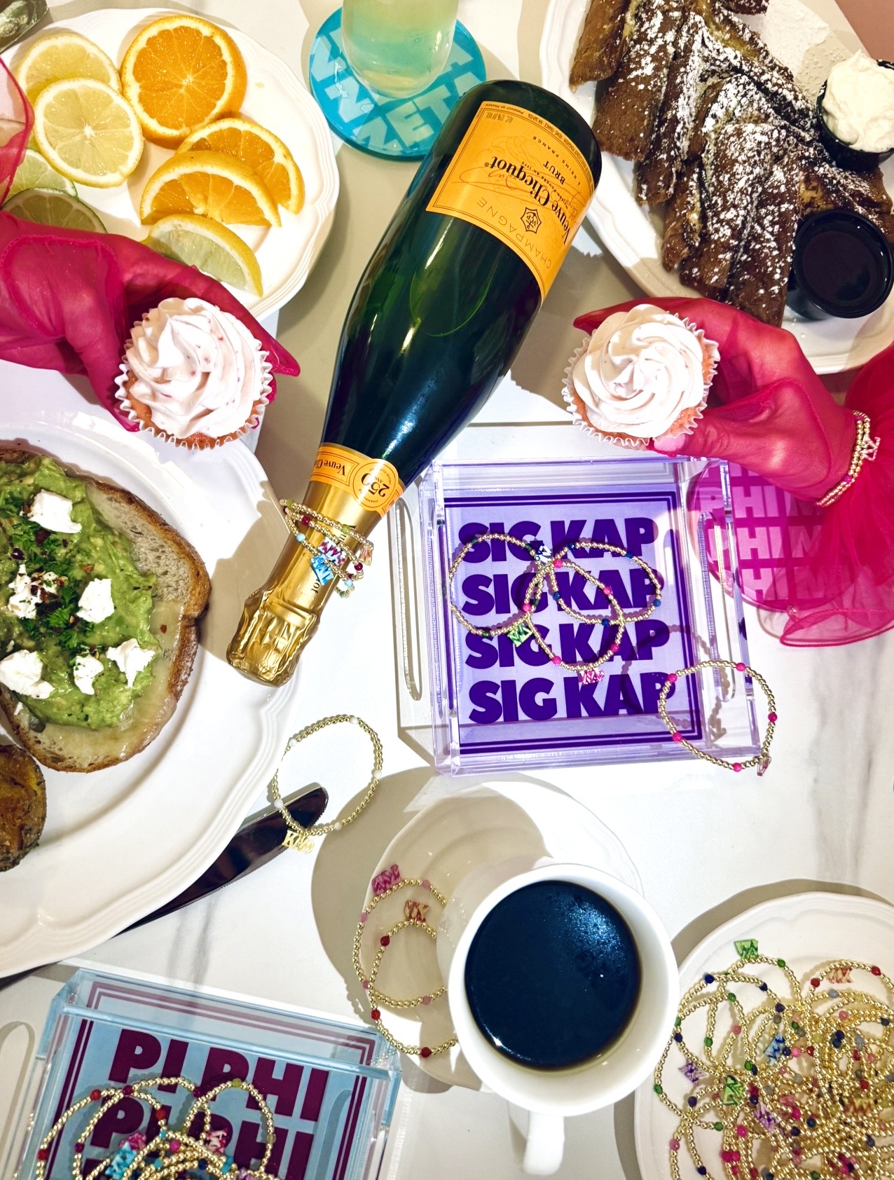 Celebration table with cake, champagne, cupcakes, and drinks, decorated with colorful items and snacks.