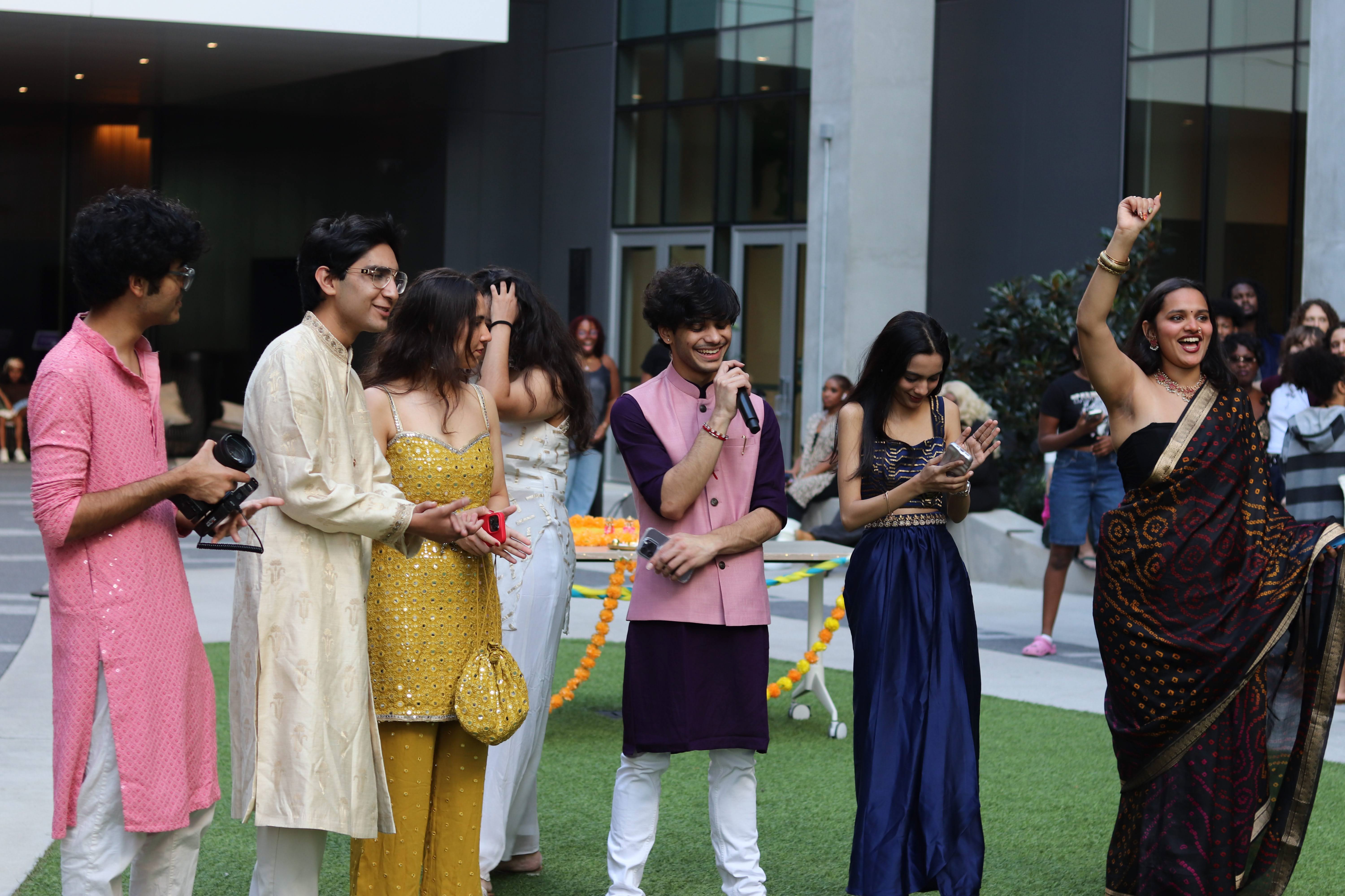 Group of people outdoors, some smiling and talking, with a modern building in the background.