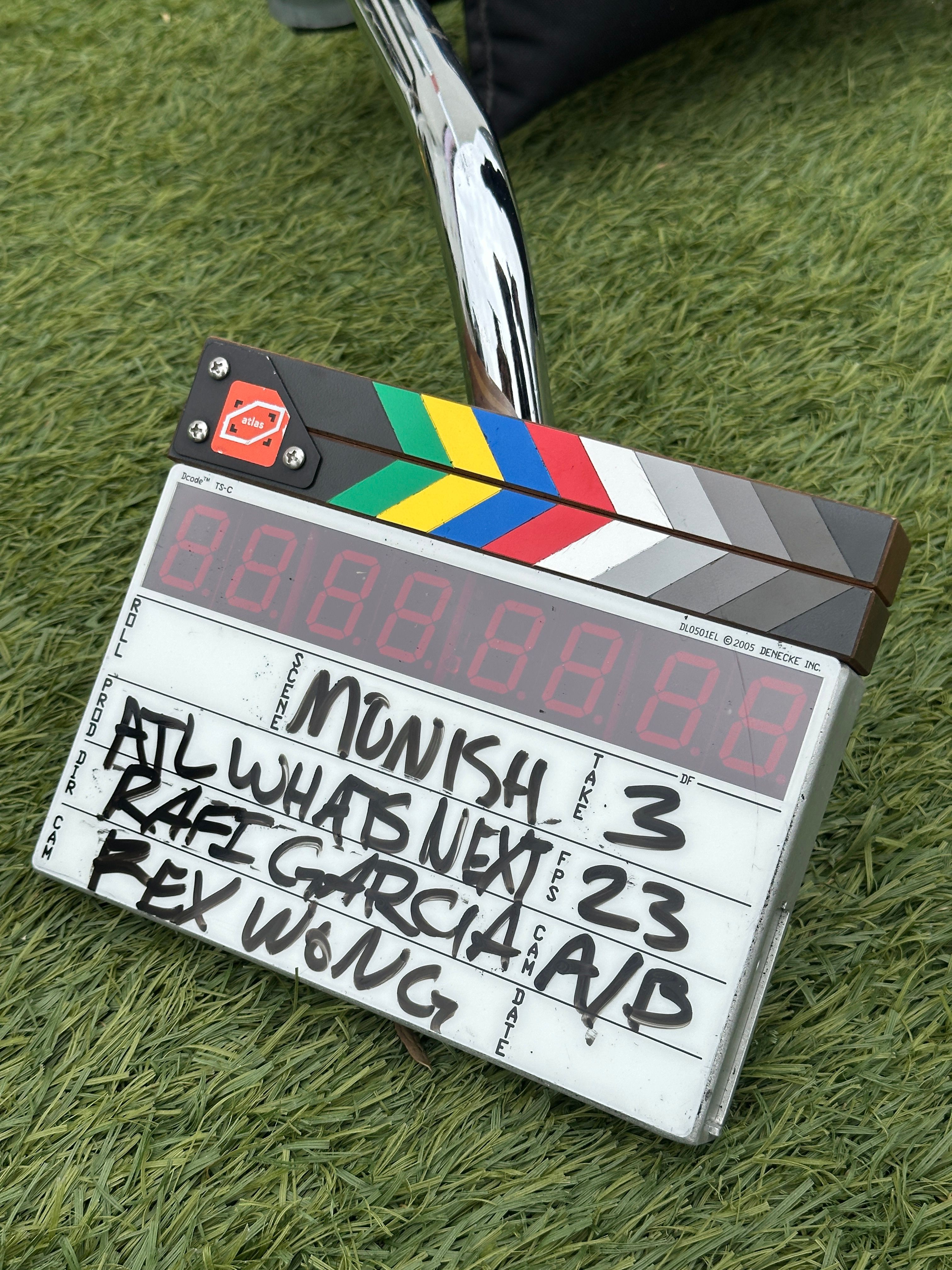 A scoreboard on grass displays names, numbers, and scores, with a colorful stripe pattern on the side.