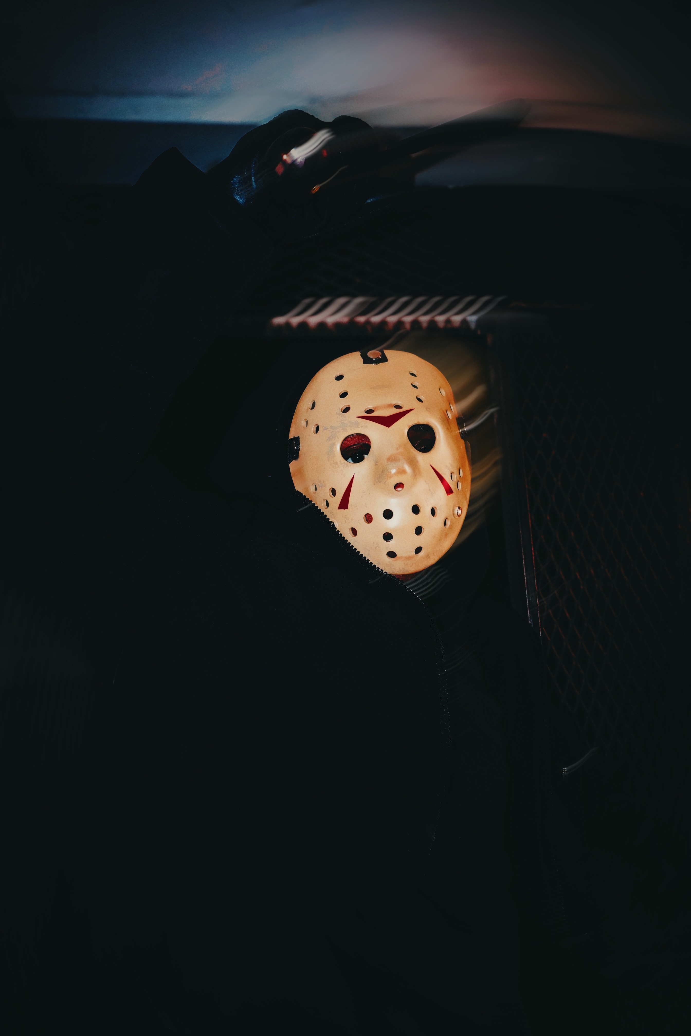 A hockey mask with red markings hangs inside a dark vehicle, with a faint light illuminating the background.