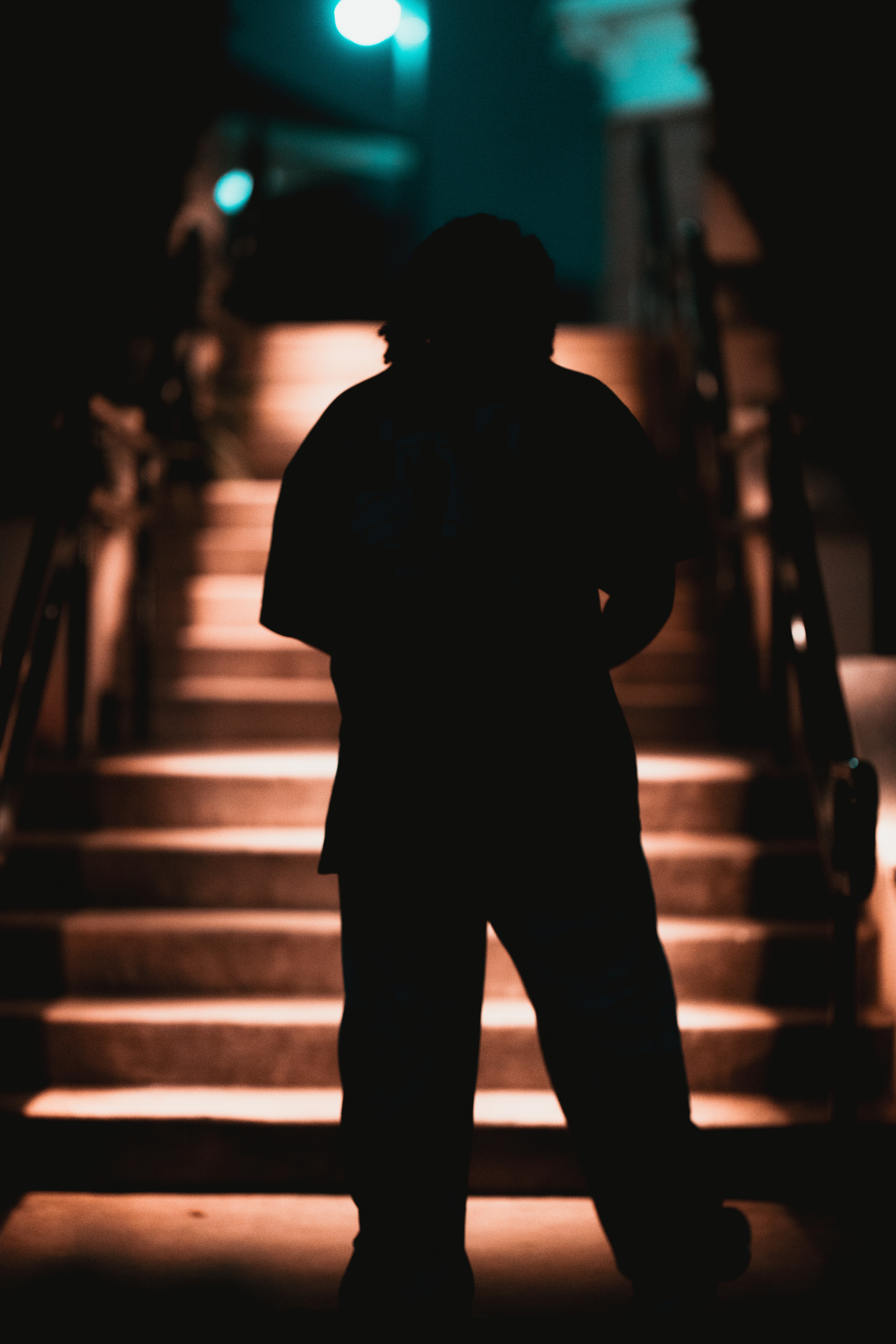 Silhouette of a person standing on illuminated stairs at night, with a ladder nearby and blurred background.