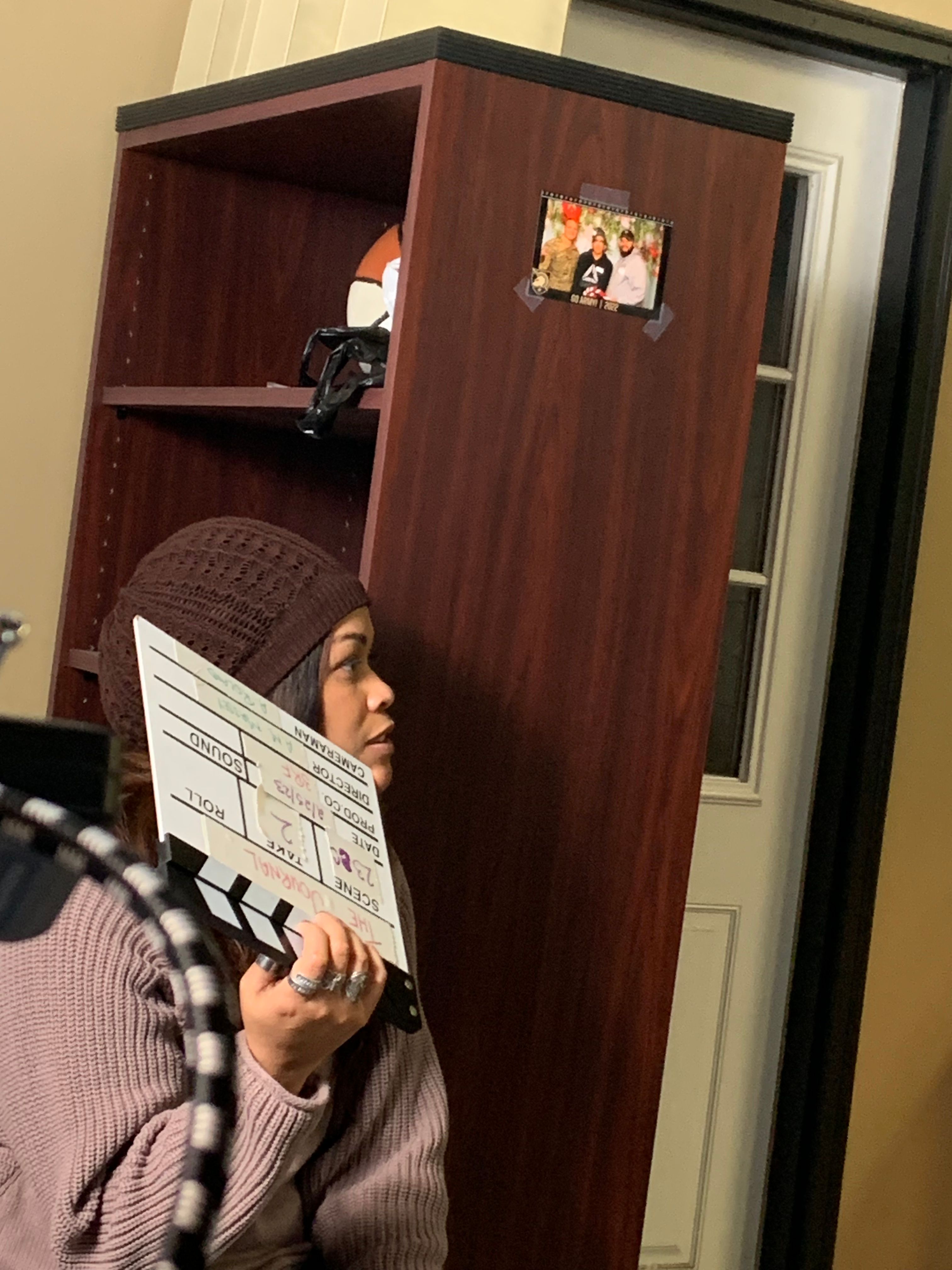 Person holding a clipboard with papers, standing in front of a wooden cabinet with open shelves.