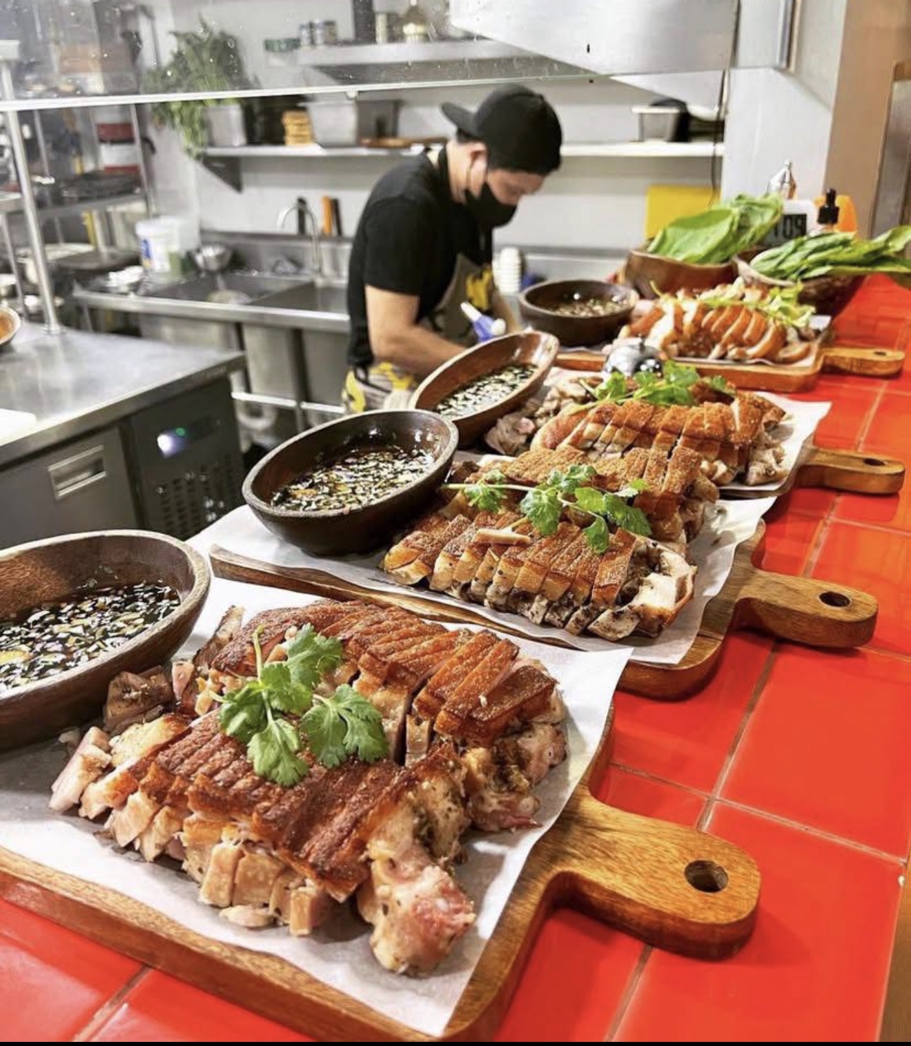 Chef preparing dishes with roasted meat and vegetables on a red-tiled counter in a kitchen.