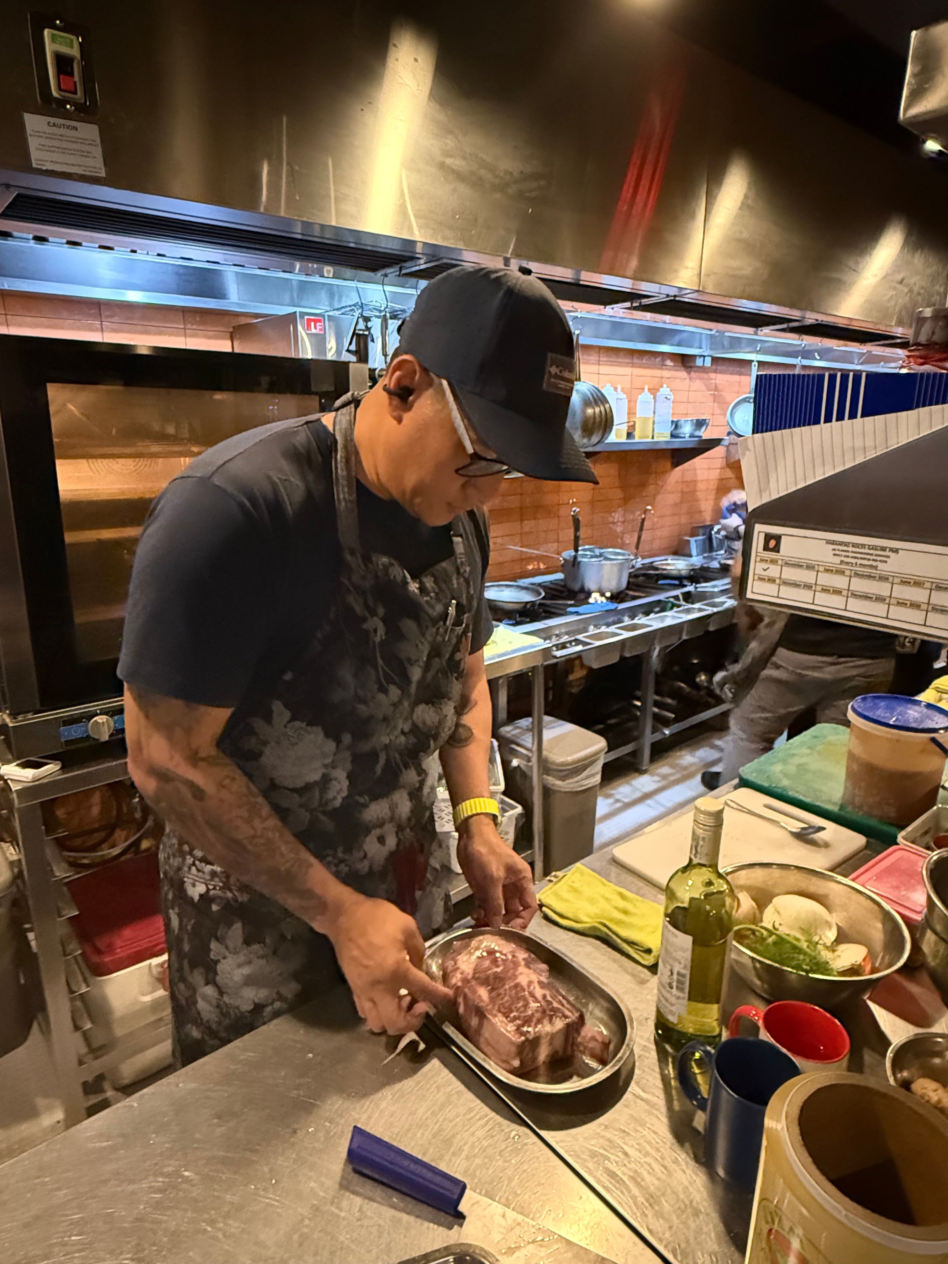 Person wearing a cap and apron, mixing ingredients in a bowl in a kitchen, surrounded by utensils and containers.