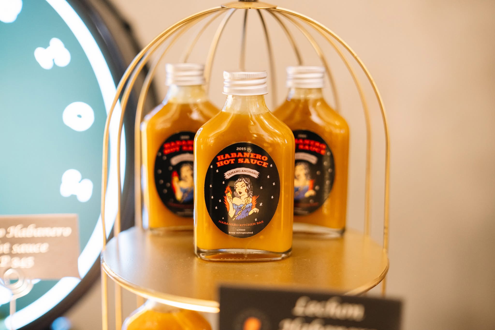 Three bottles with orange liquid on a round gold stand, label features a cartoon character and text, background is beige.