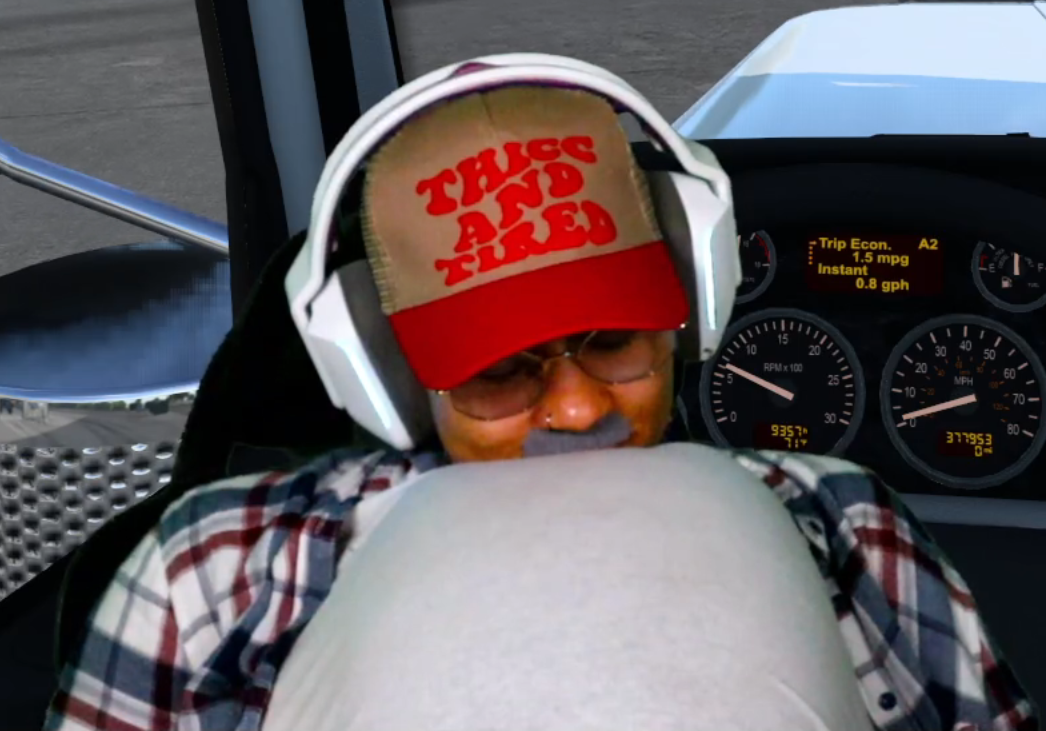 Person wearing a red and beige cap, sunglasses, and headphones, sitting in a vehicle with dashboard visible.