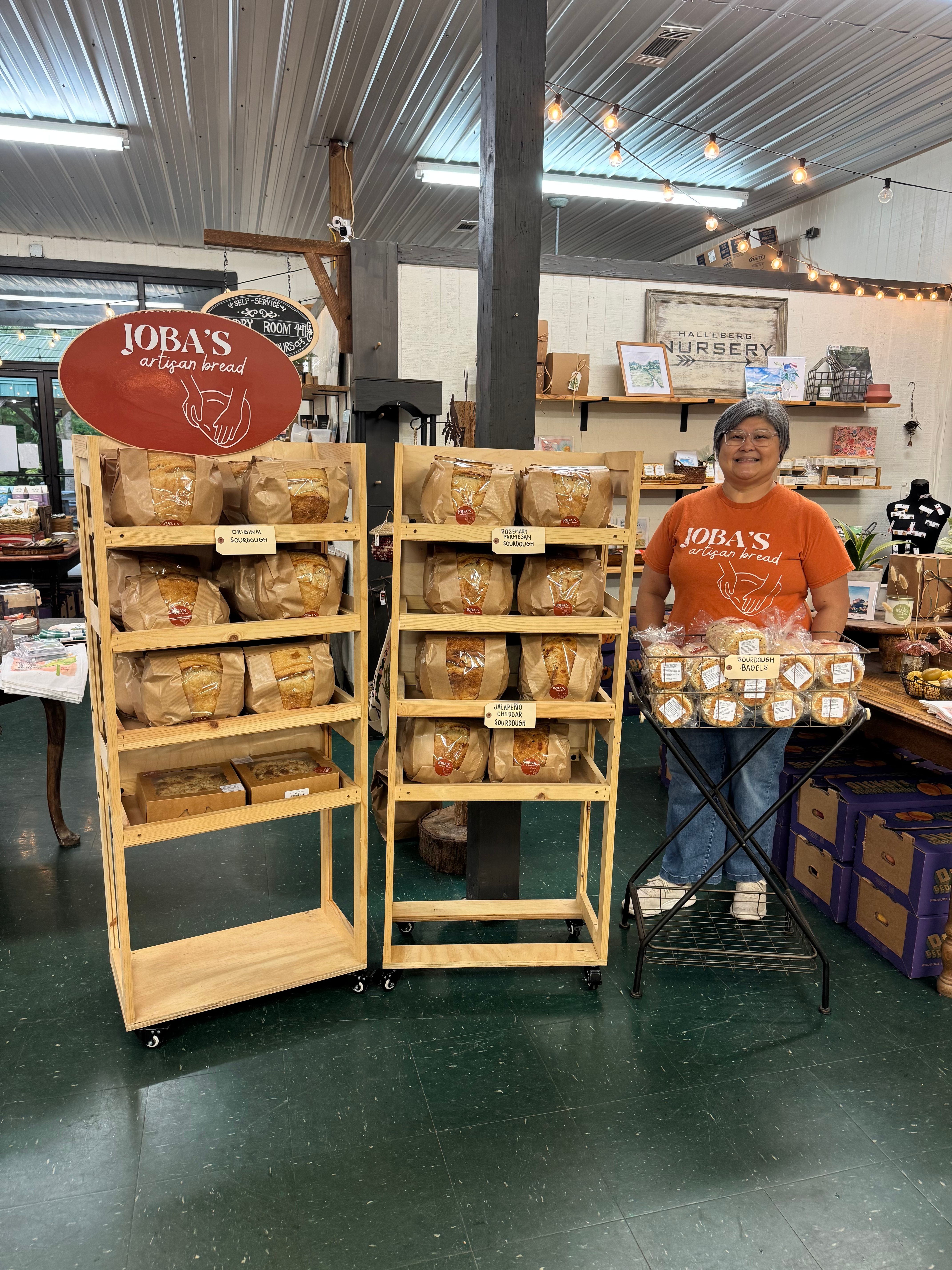 Person standing behind a wooden display shelf with bread in a store, with a red sign reading 'Toys' nearby.