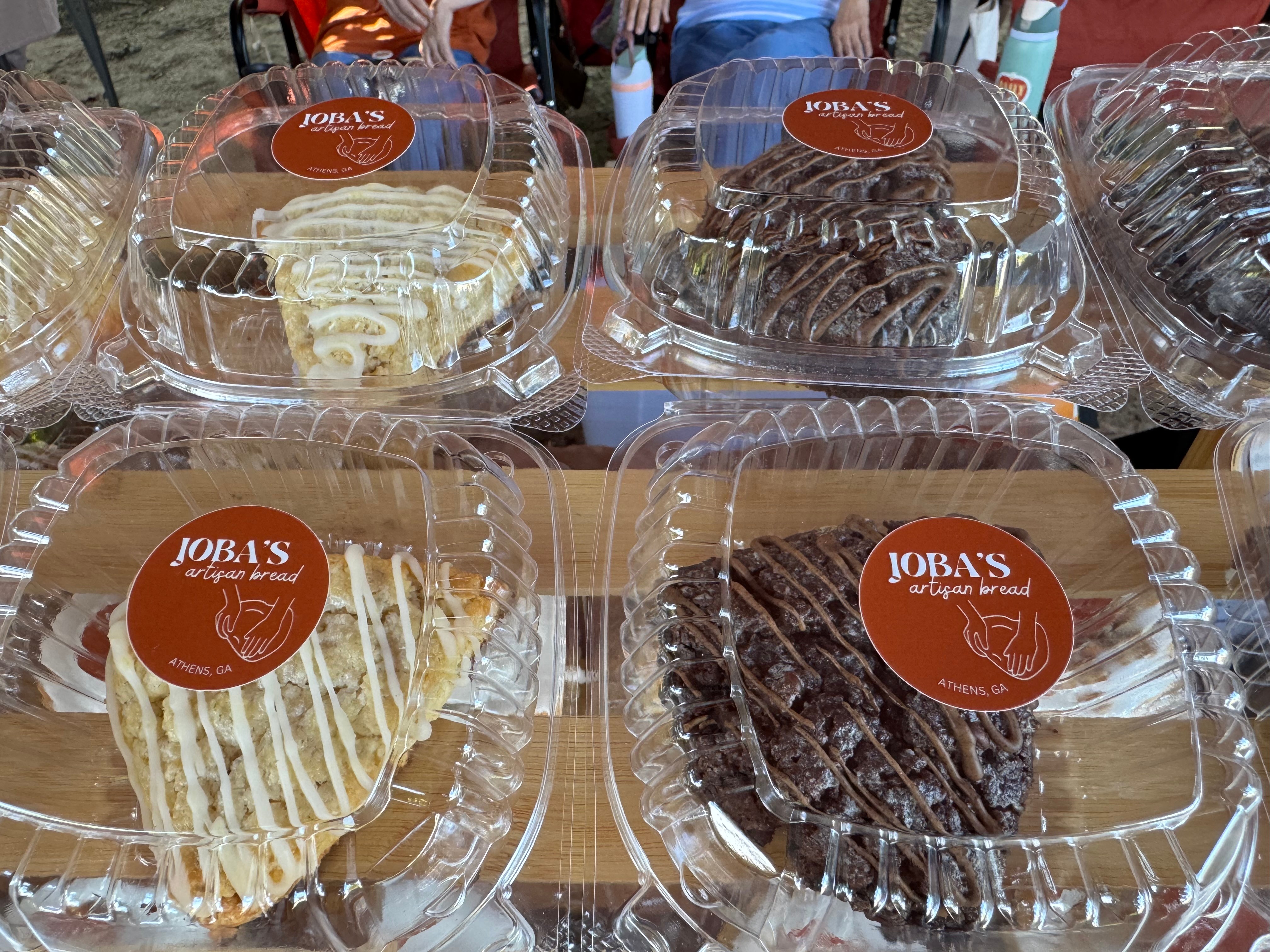 Four slices of cake in clear plastic containers, two with white frosting and two with chocolate frosting, on a table.