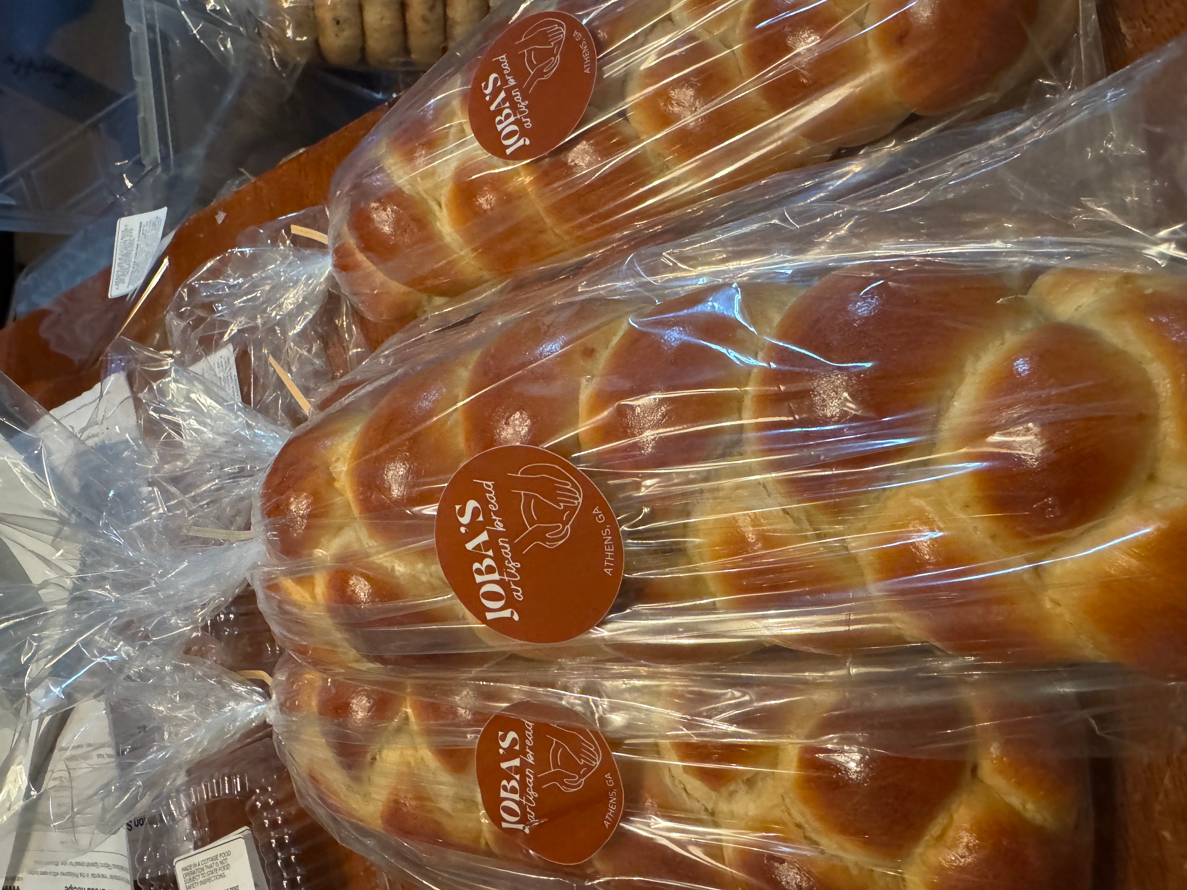 Loaves of bread wrapped in clear plastic with orange labels, displayed on a surface.