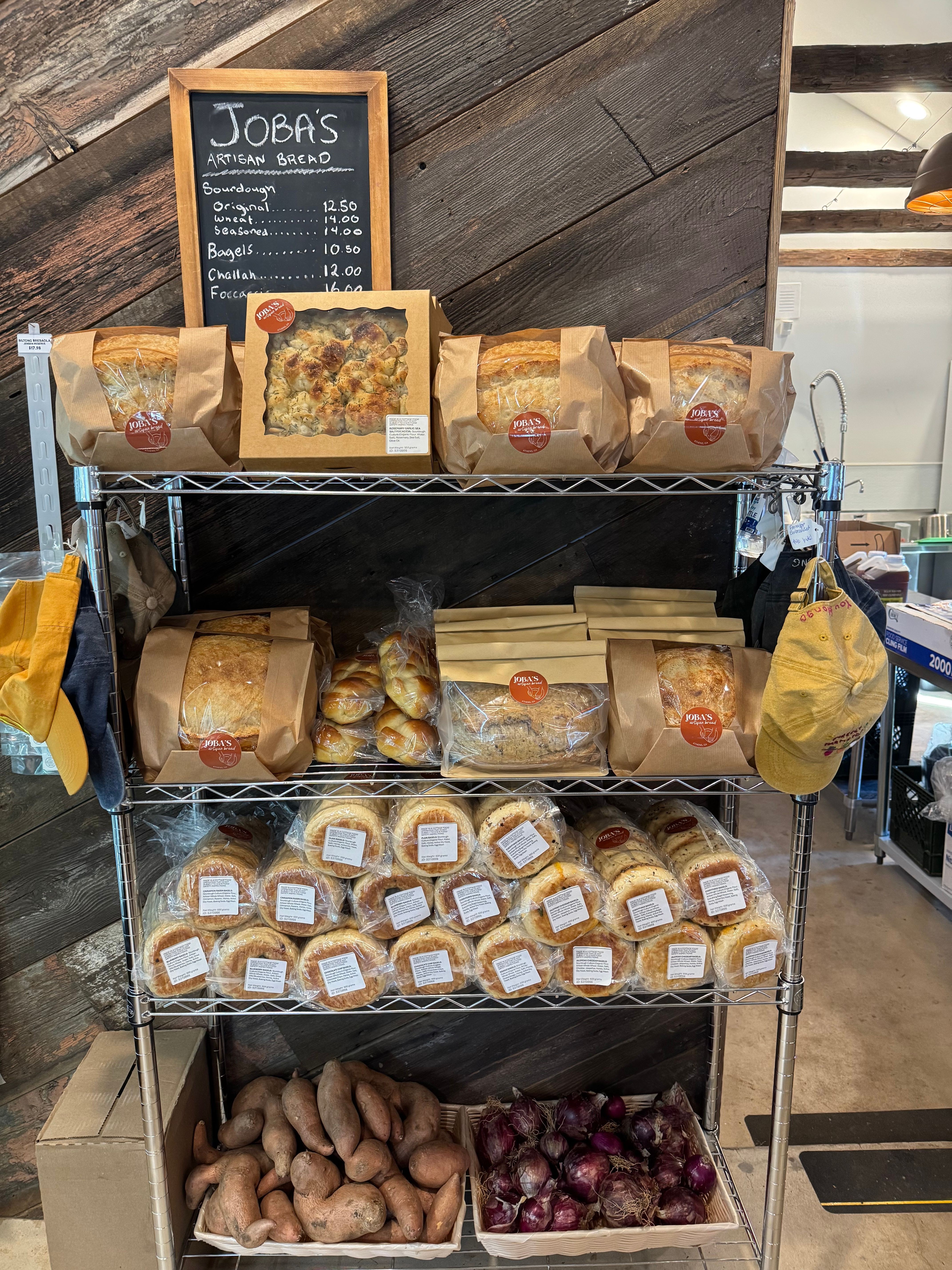 Display of baked goods, jars of jam, and fresh ginger on a metal rack at a market stall.