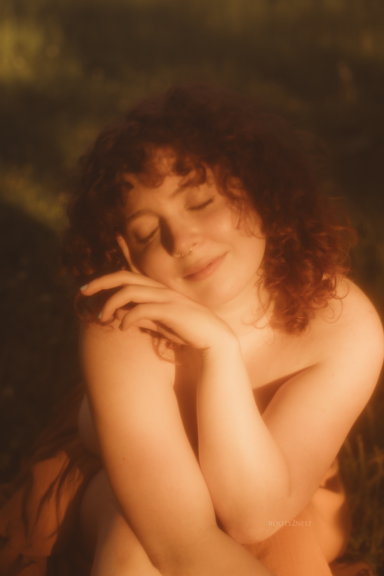 A woman with curly hair and closed eyes smiling gently, resting her face on her hand.
