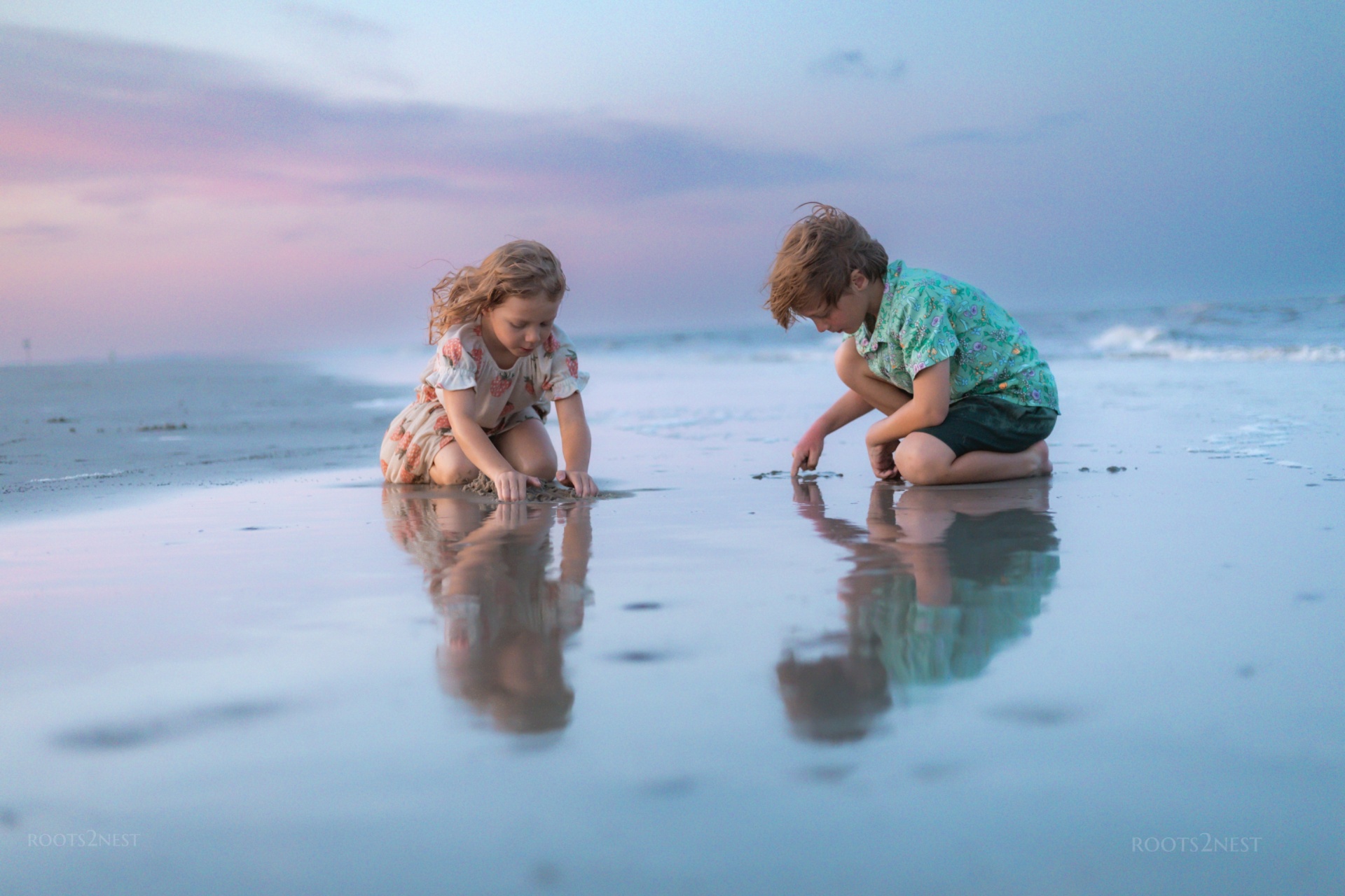 Two children playing in shallow water at the beach during sunset, with reflections on the wet sand.