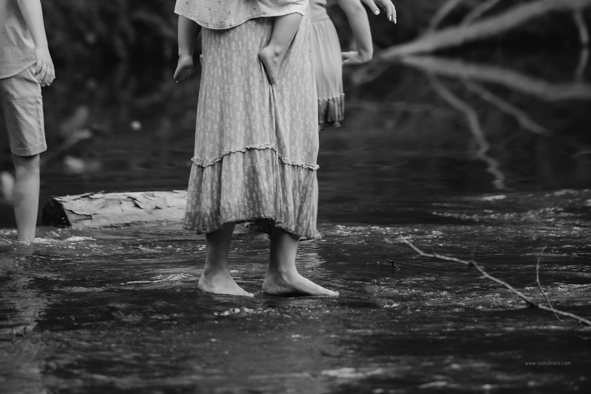 Person standing in water wearing a long skirt, with other people partially visible nearby, in a natural setting.