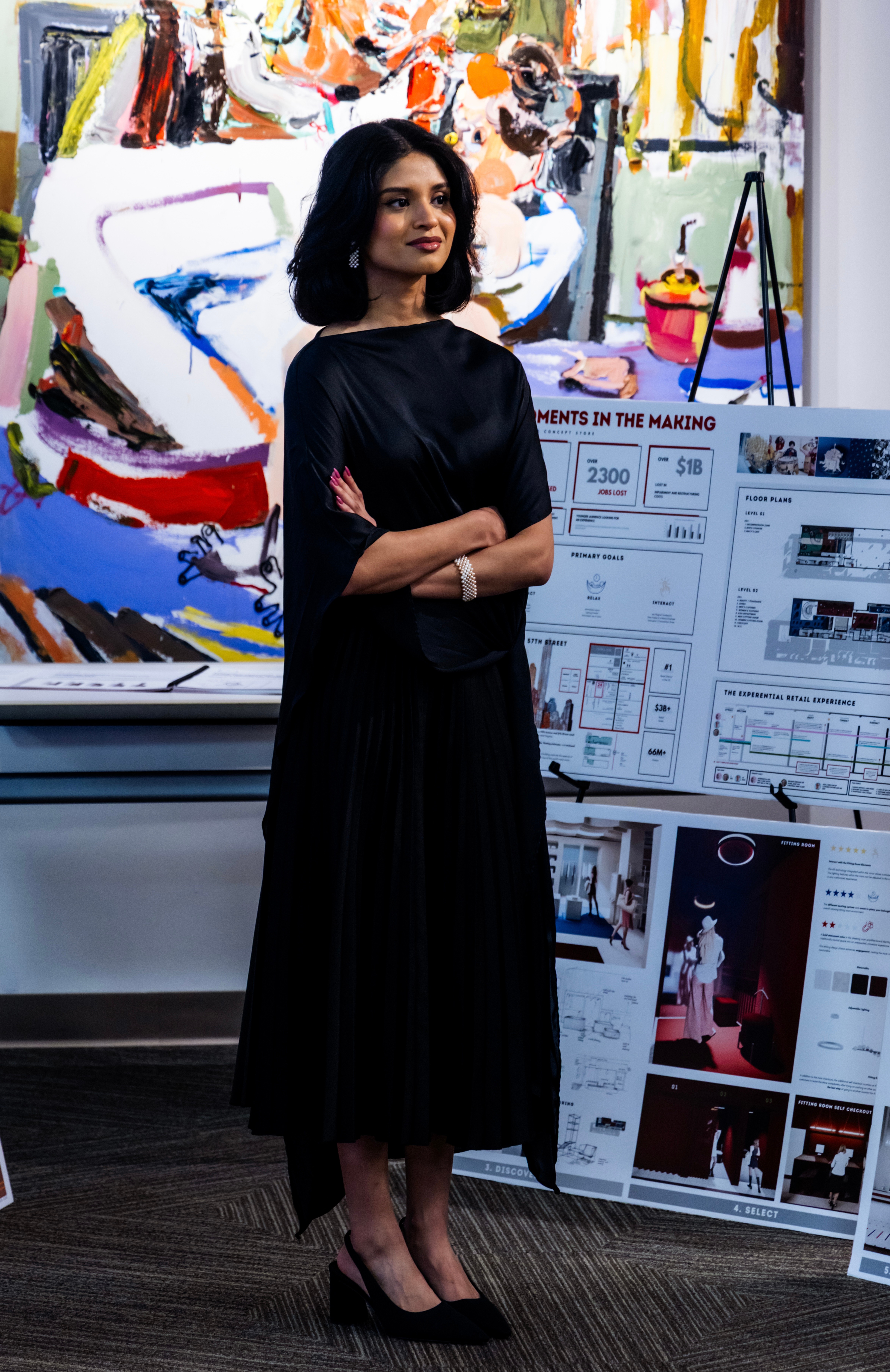 Woman in black dress standing with arms crossed in front of colorful abstract artwork and display boards.