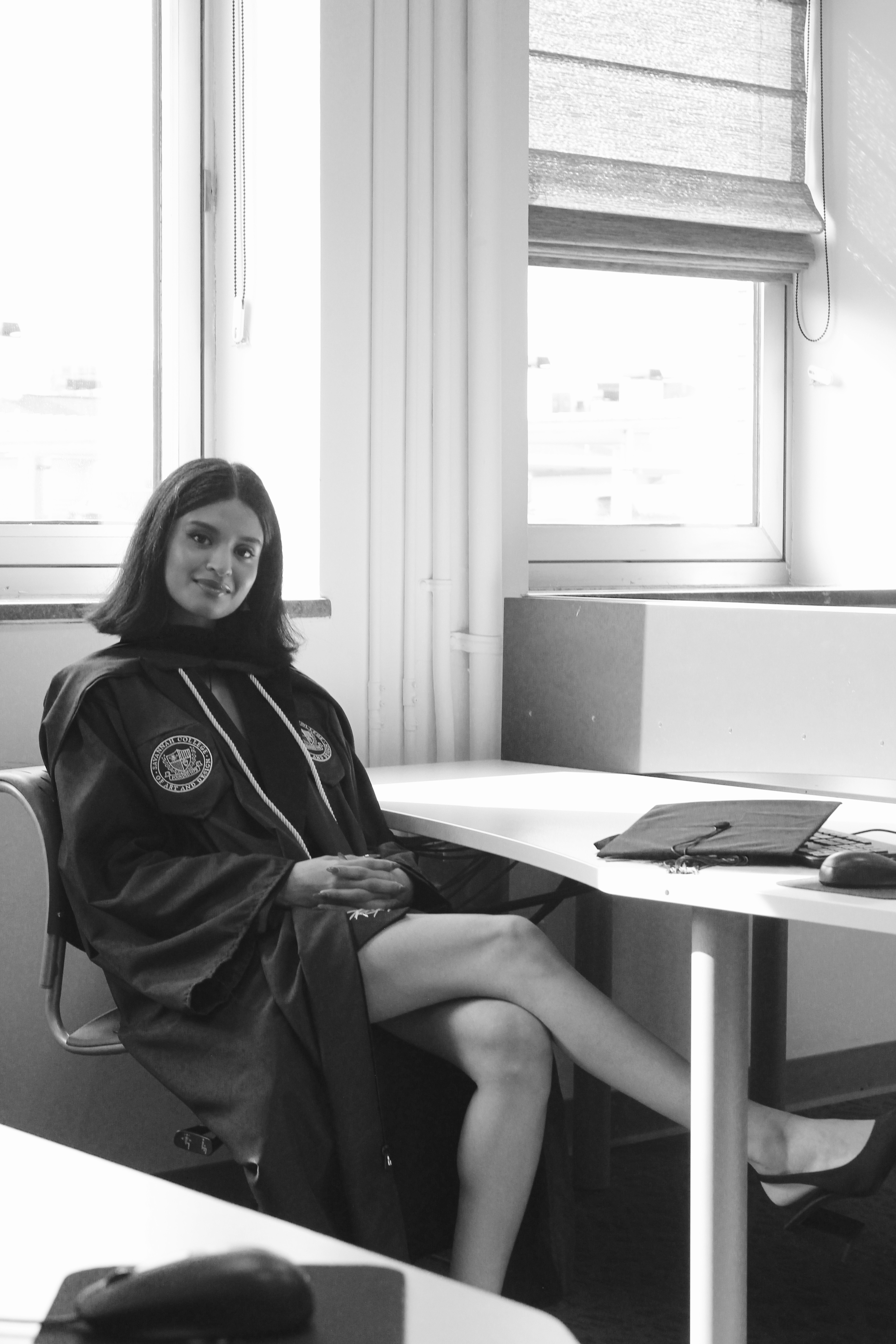 Woman sitting at a desk near windows, smiling, with a laptop and papers, in a bright room.