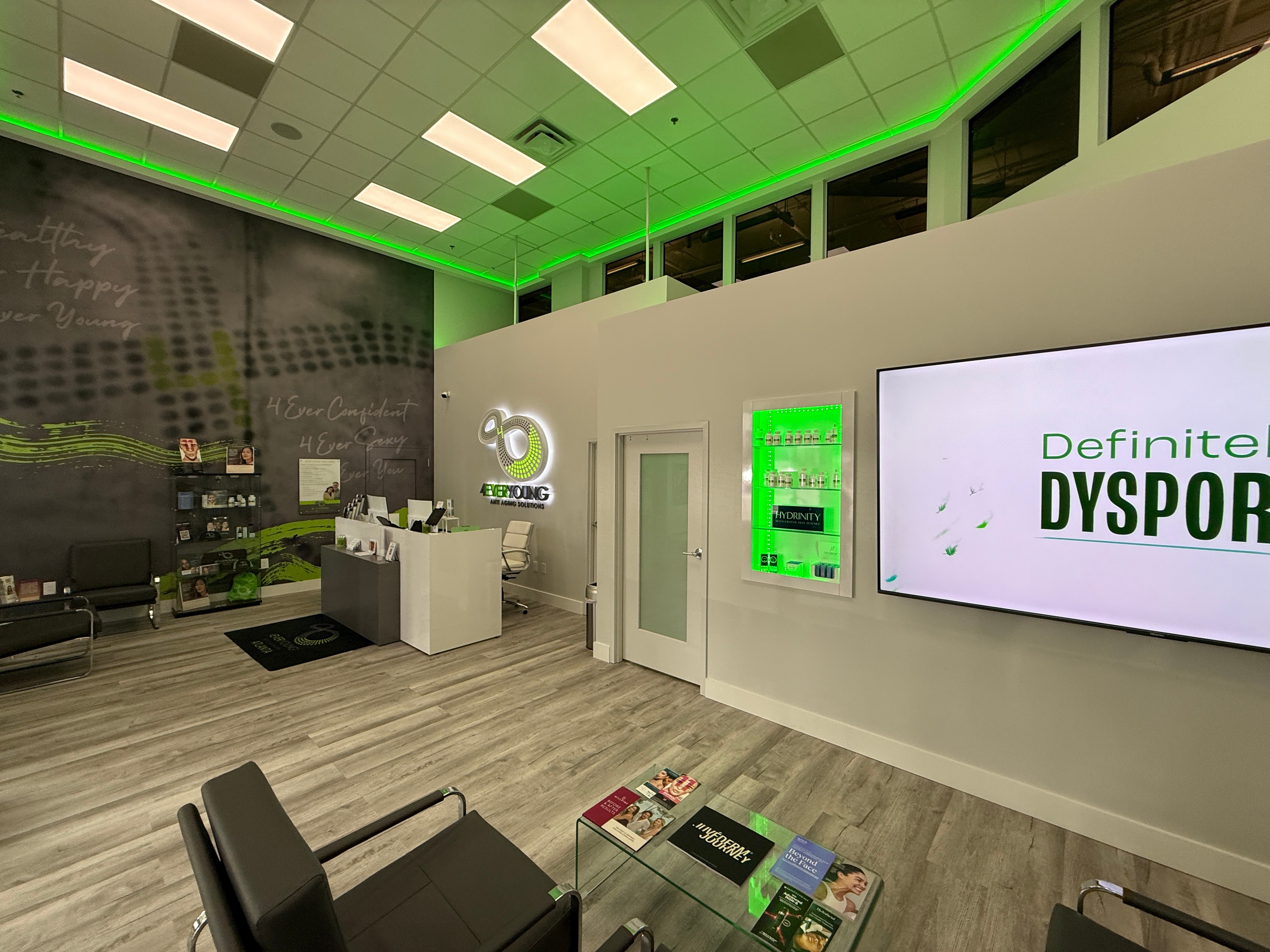 Modern waiting area with a reception desk, digital screens, and seating, illuminated by green accent lighting on the ceiling.
